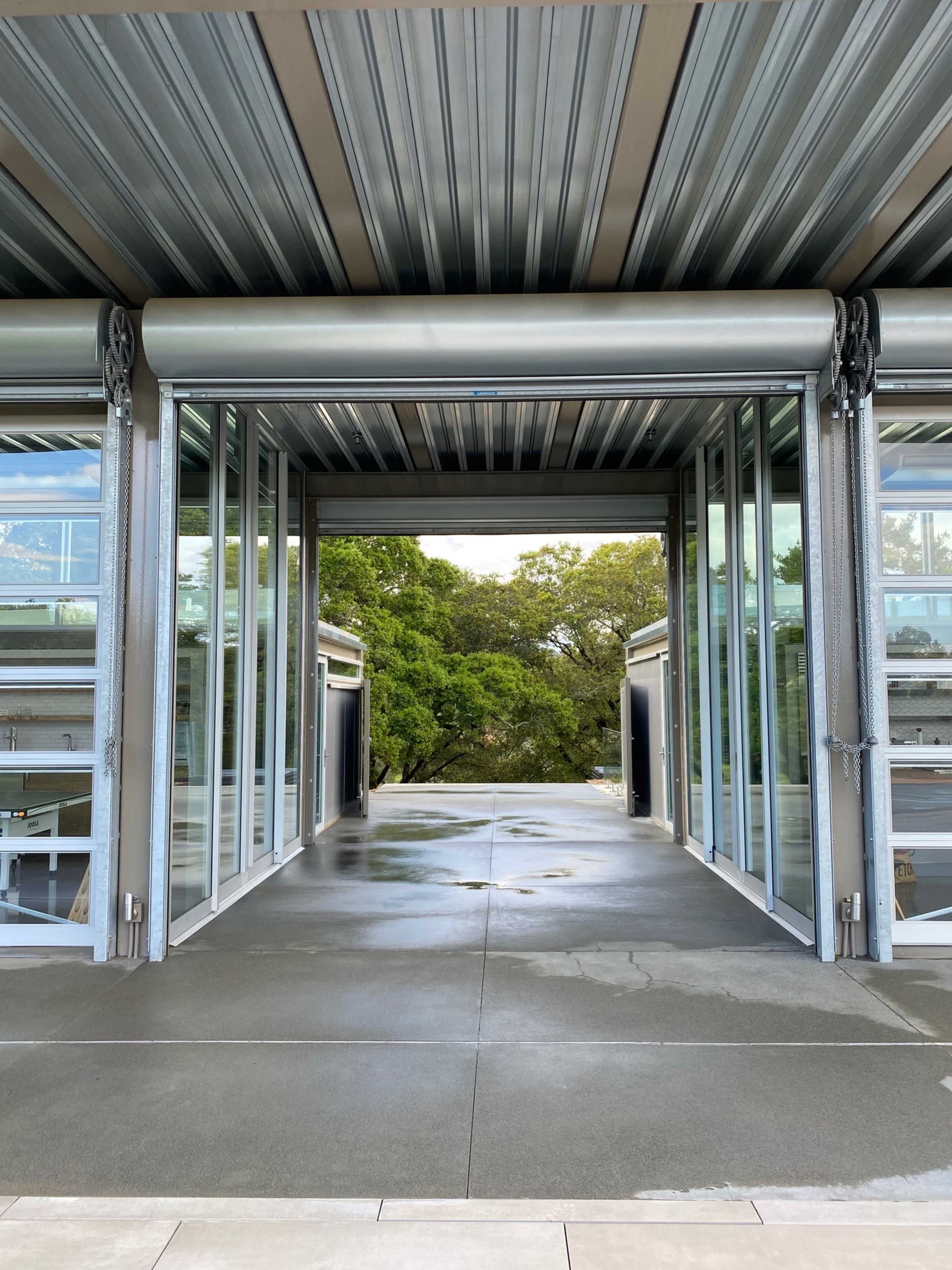 A modern architectural space with large glass doors opening to an outdoor area surrounded by trees.