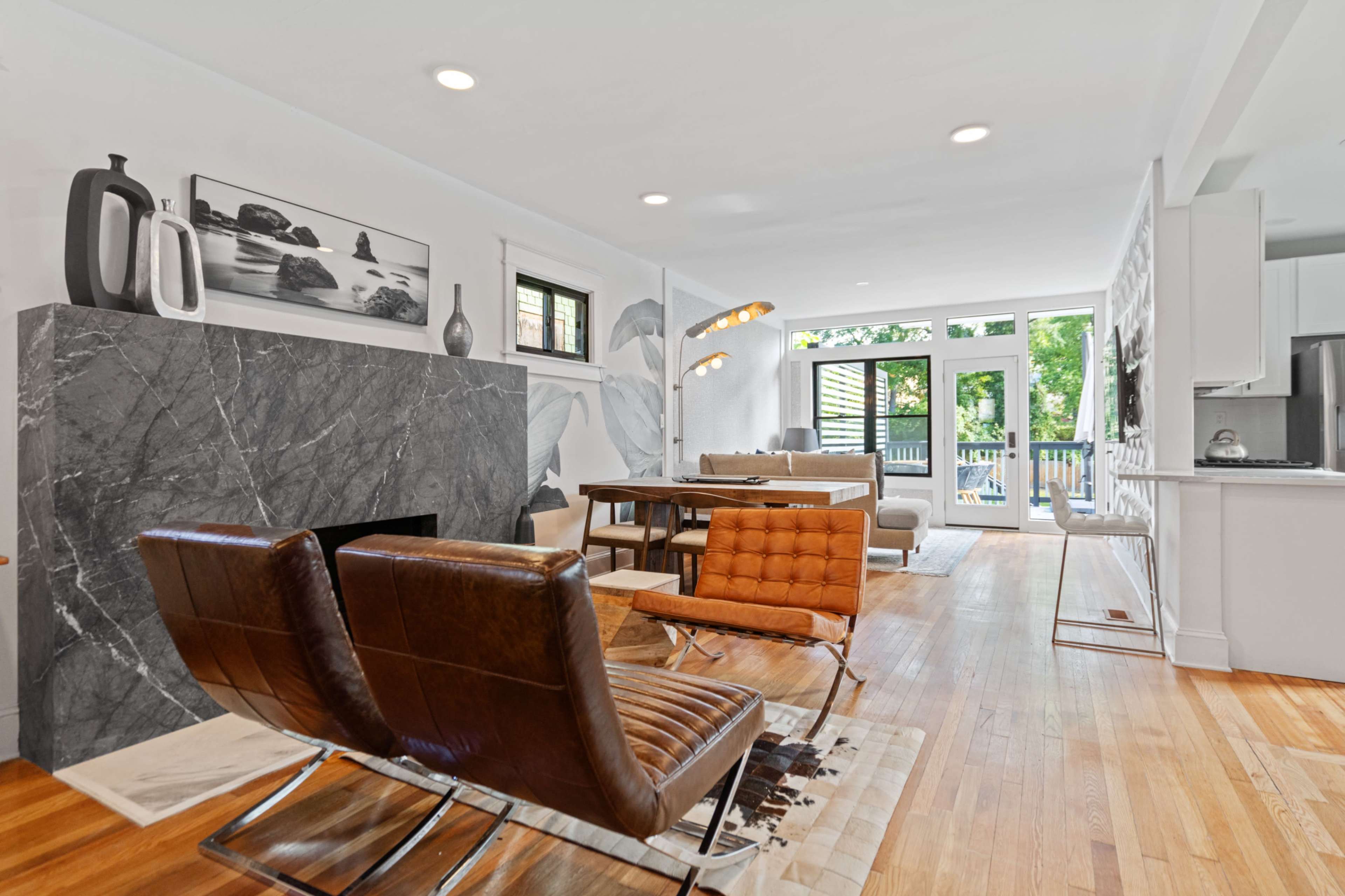 A modern living room with a marble fireplace, a dining table, and large windows leading to a balcony.