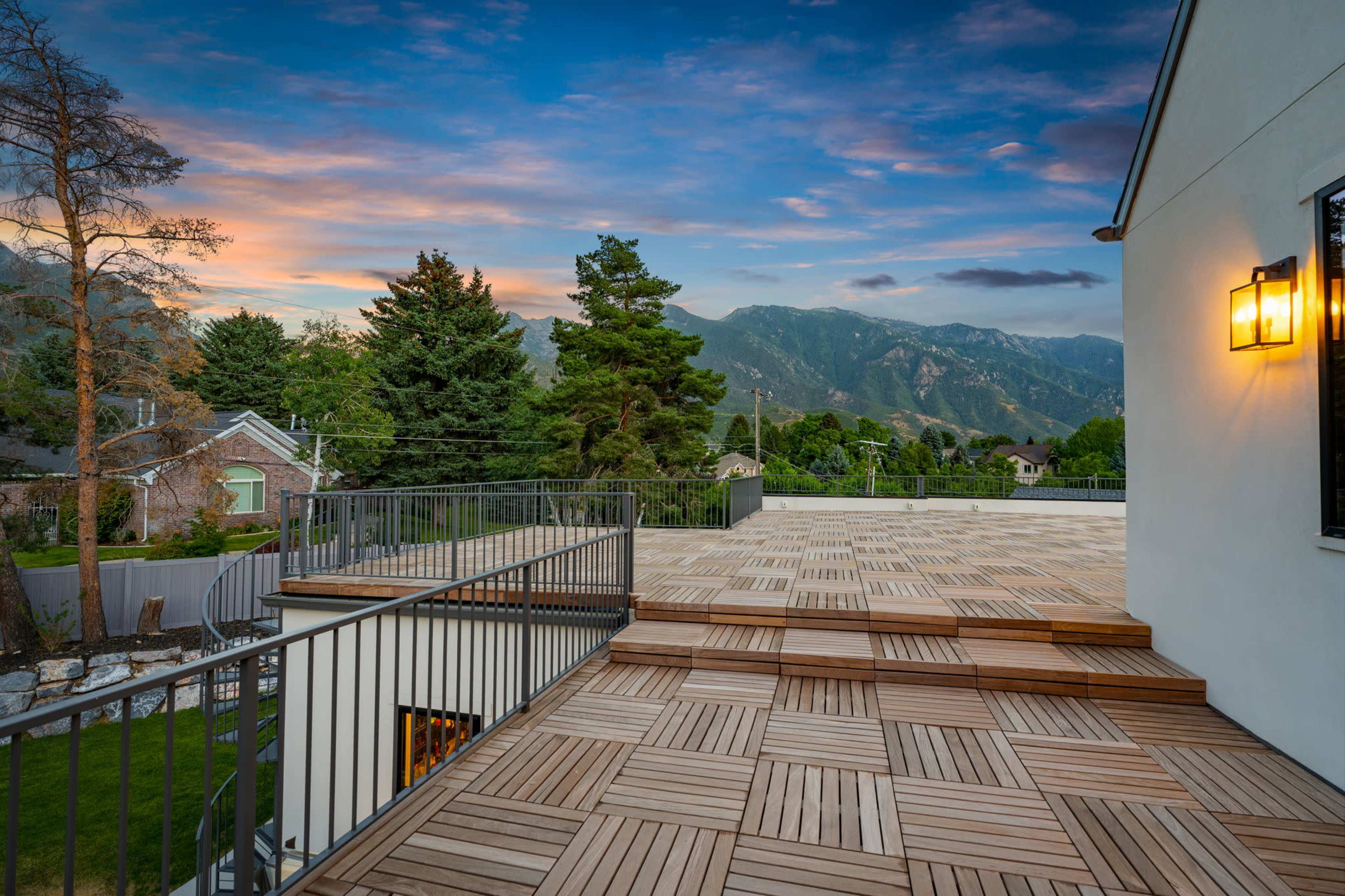 The image shows a wooden deck overlooking a scenic landscape with mountains and trees during sunset.