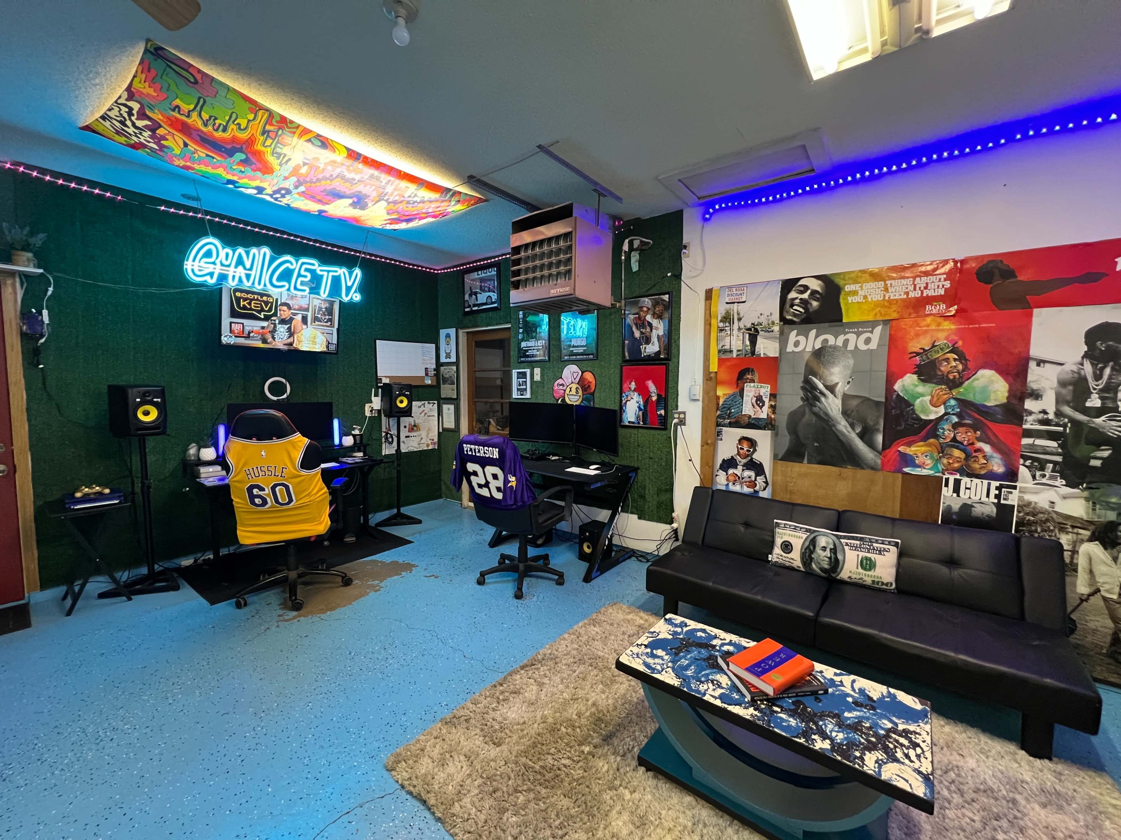 The image shows a vibrant media room with two office chairs, a couch with decorative pillows, a coffee table, and a wall adorned with posters and neon lights.