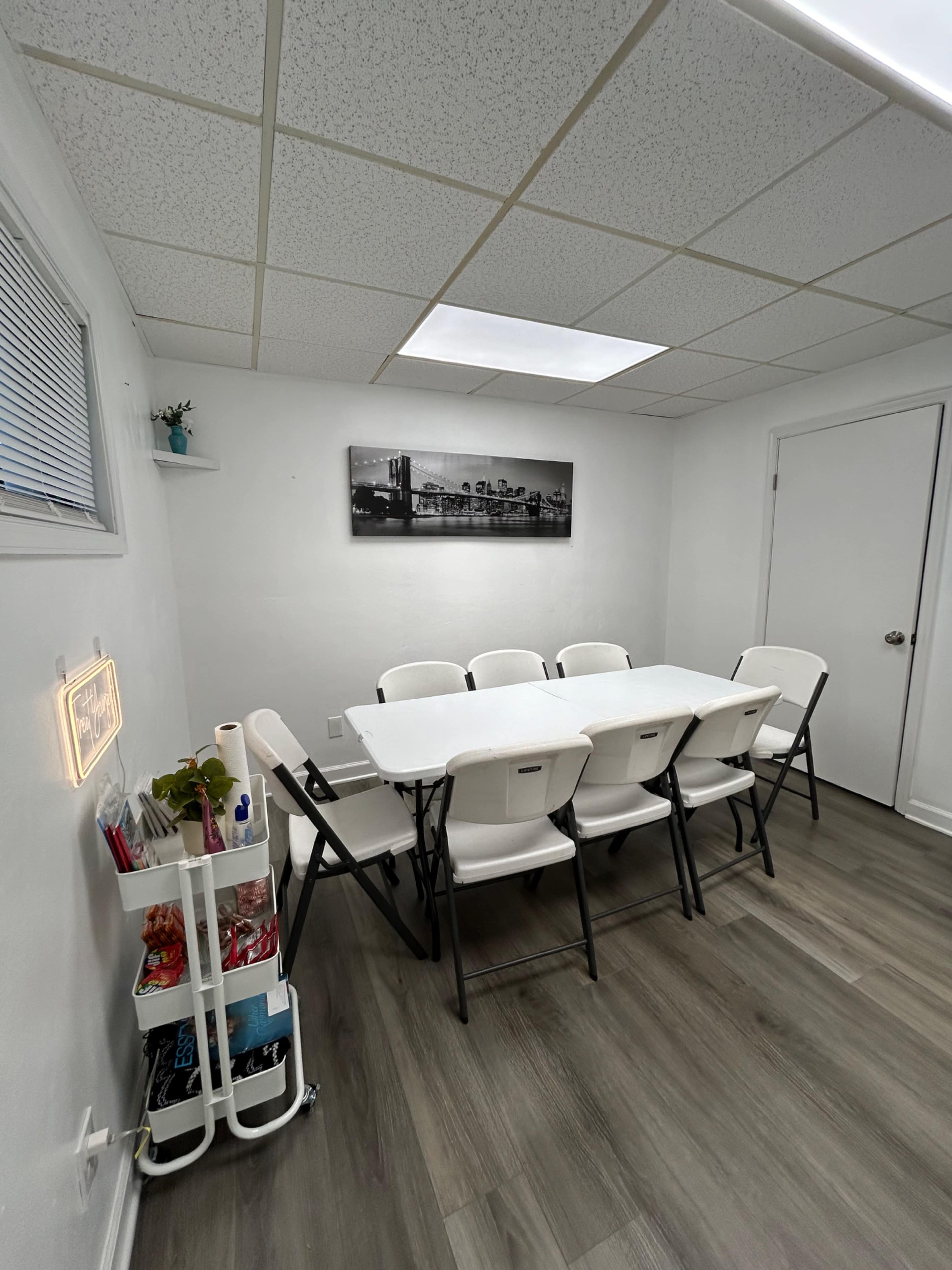 A conference room is set up with a long table surrounded by folding chairs under bright overhead lights.
