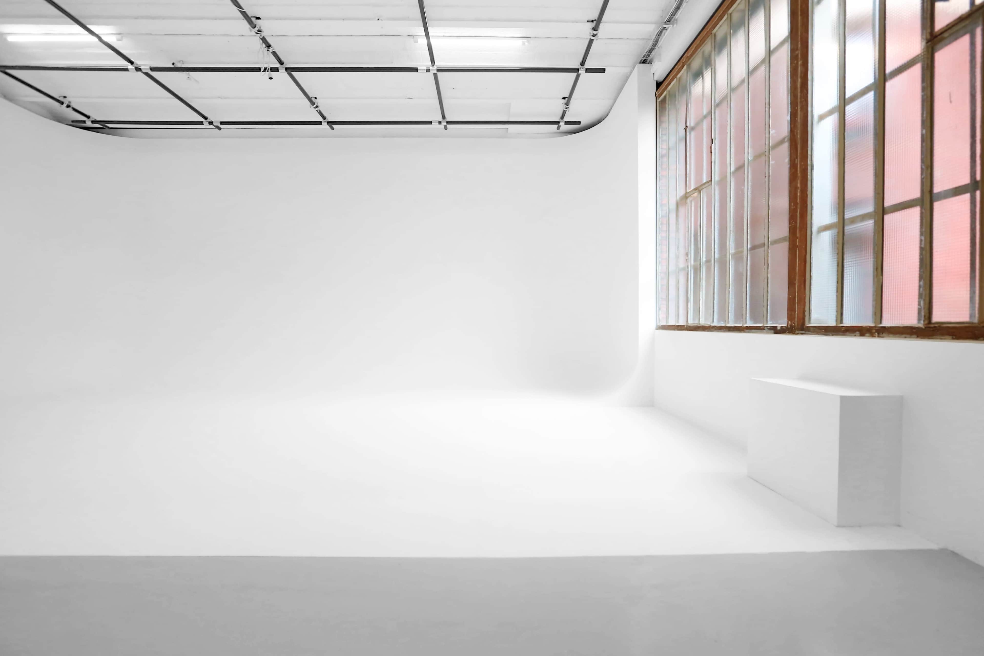 A bright, empty studio space features white walls, a smooth floor, and large windows allowing natural light.