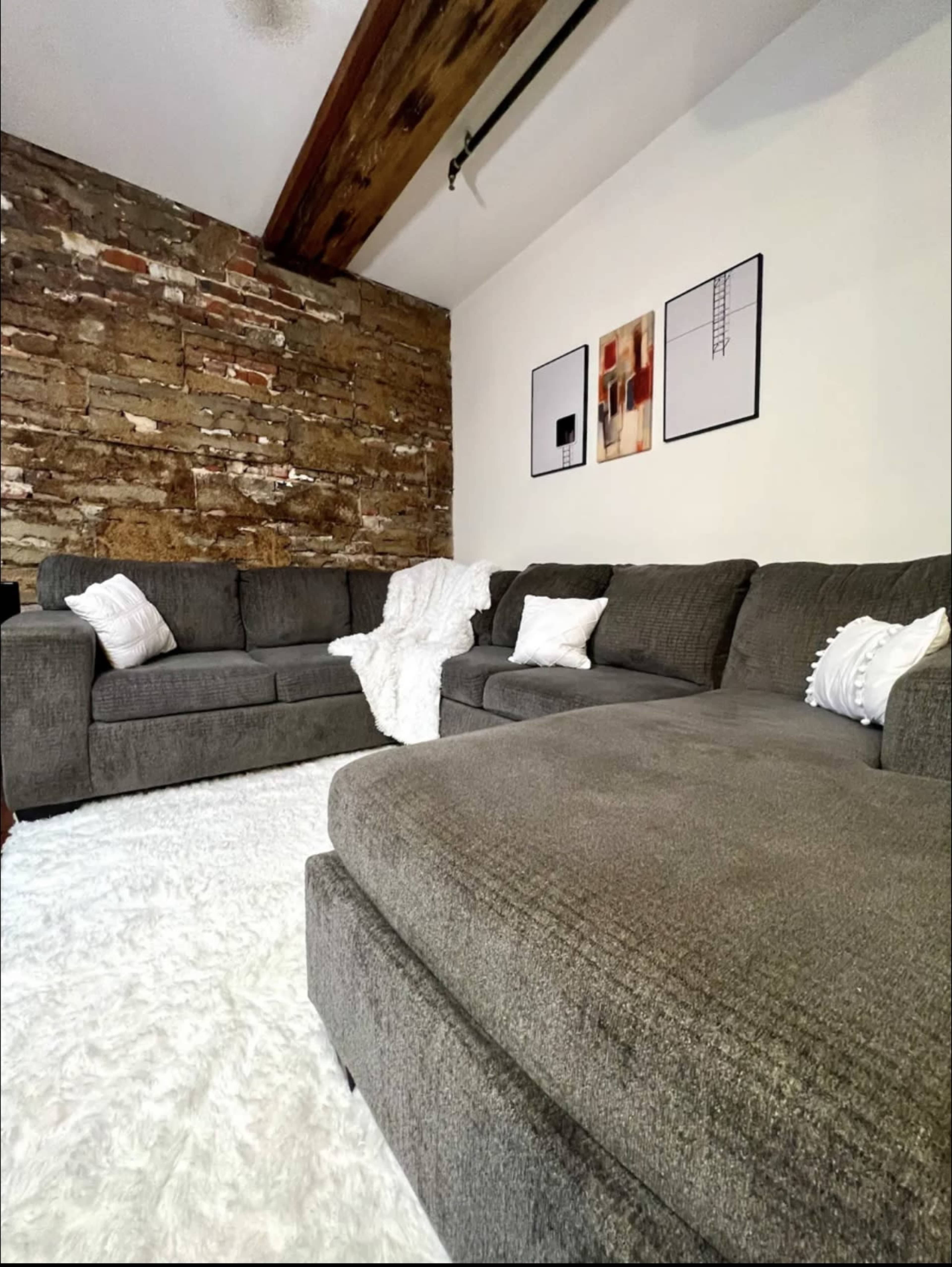 A cozy living room features a sectional sofa and two armchairs placed on a plush rug against a rustic stone wall.