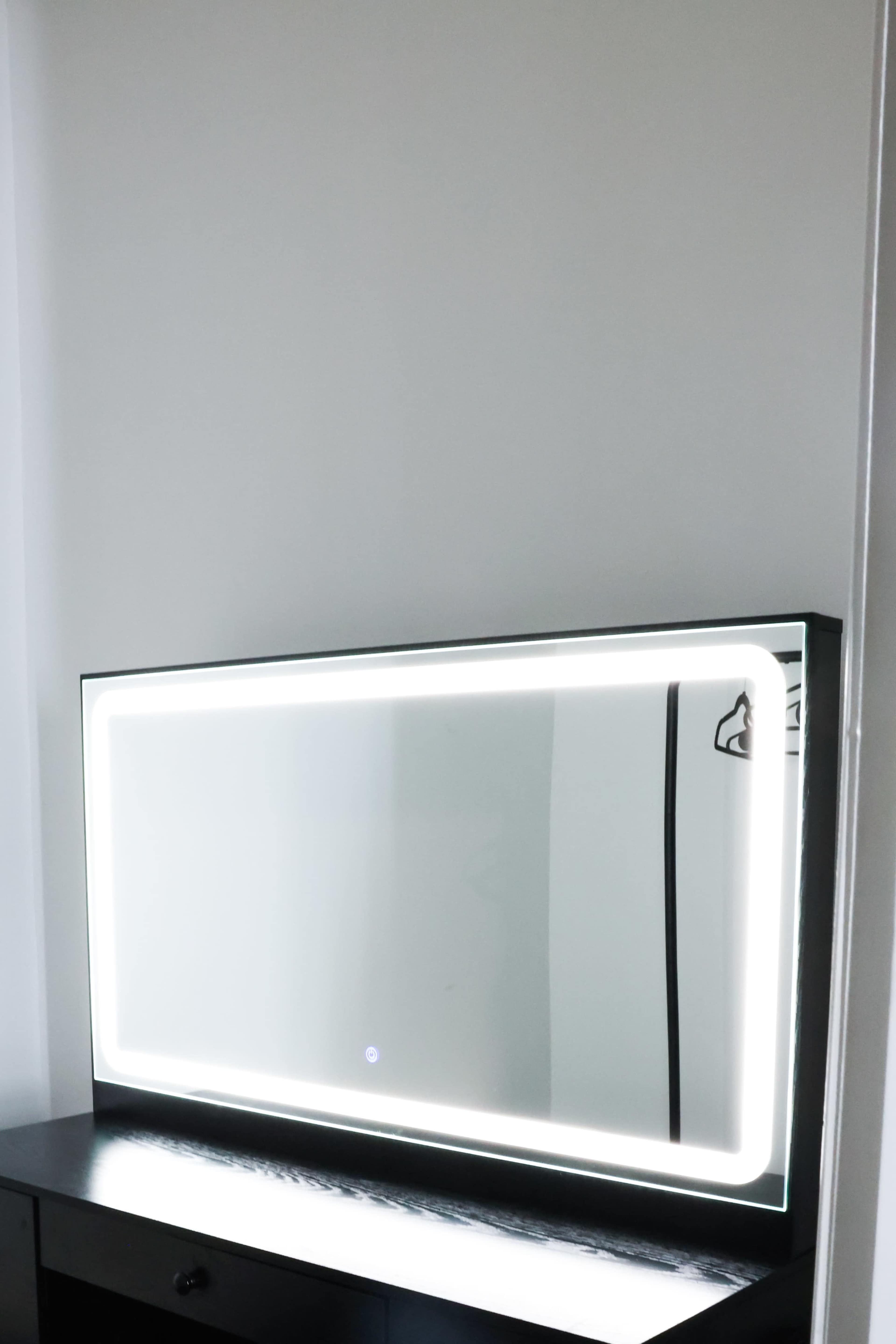A backlit mirror is mounted on a white wall above a black dresser.