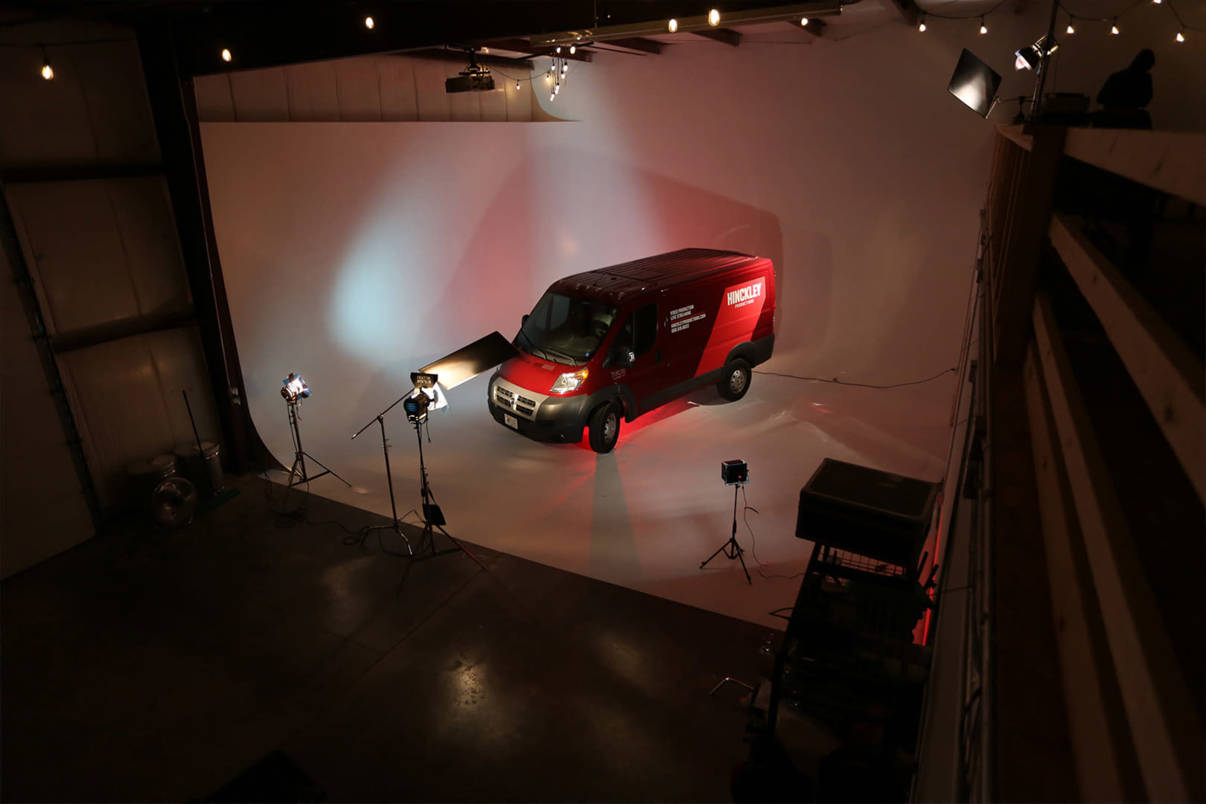 A red van is positioned on a white backdrop in a well-lit studio space, surrounded by studio lights and equipment.