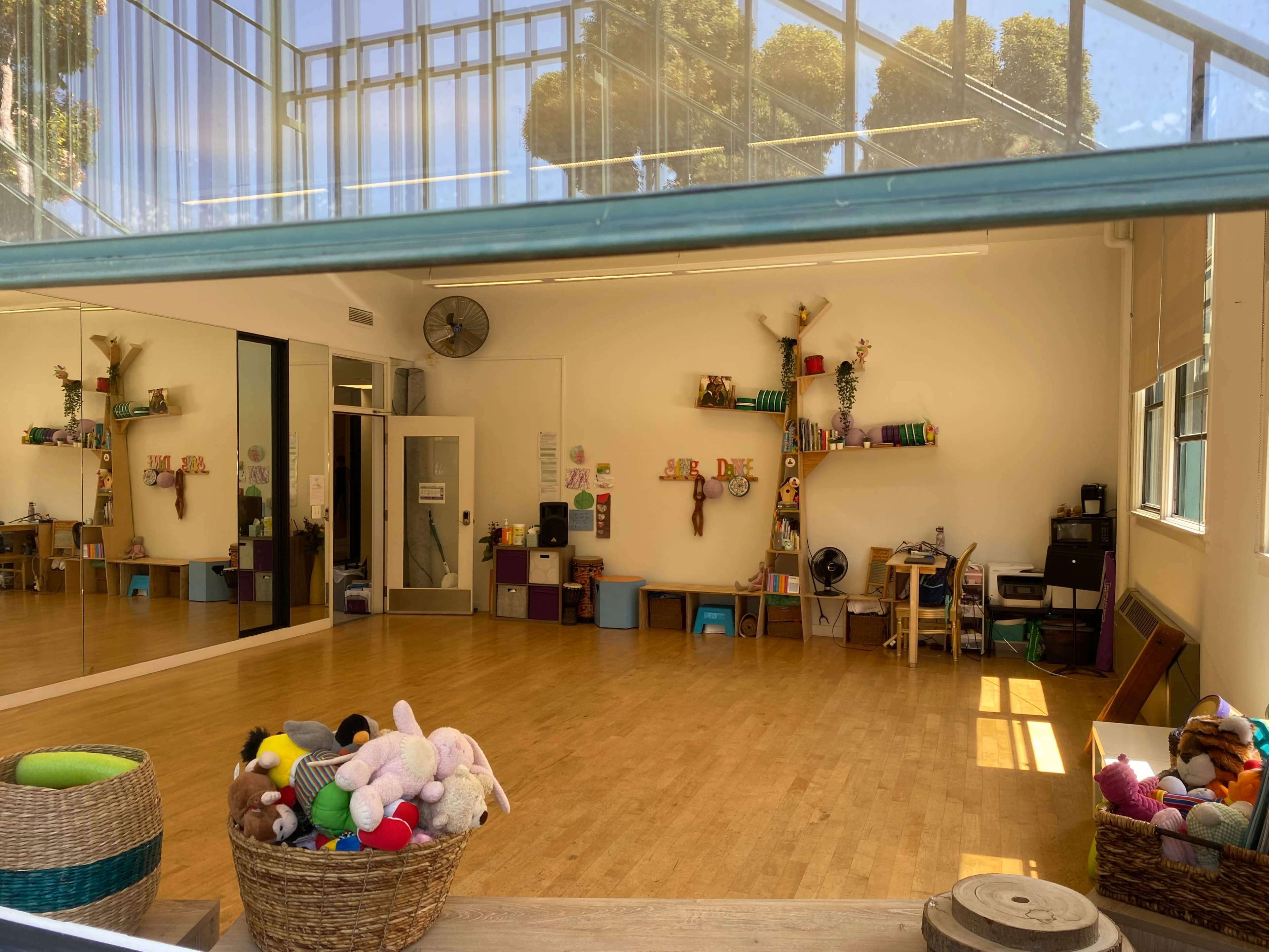 A bright, spacious room with wooden flooring, shelves decorated with colorful items, and a basket filled with stuffed animals in the foreground.