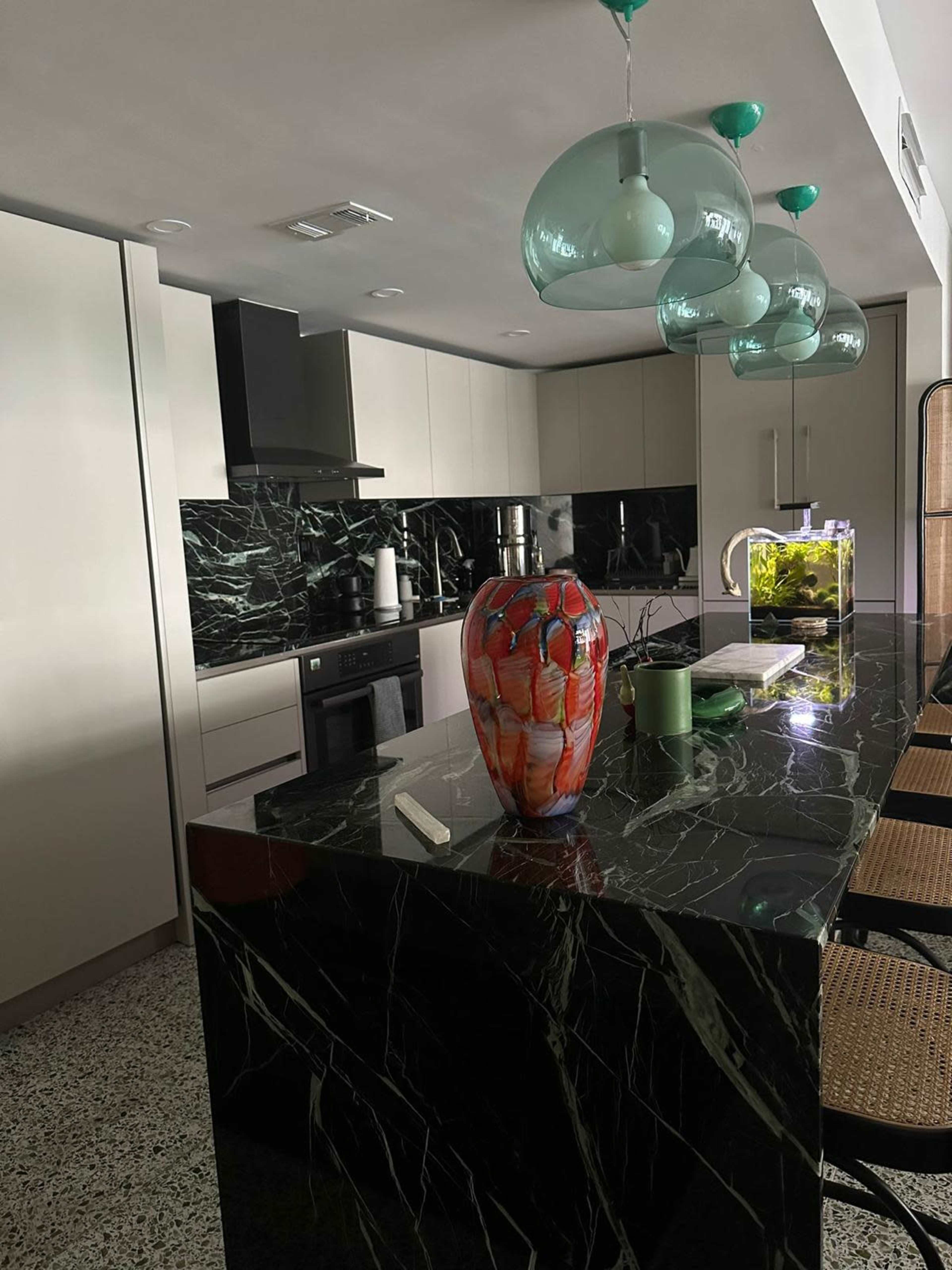 A modern kitchen with a black marble countertop, green decorative elements, and three glass pendant lights hanging above.