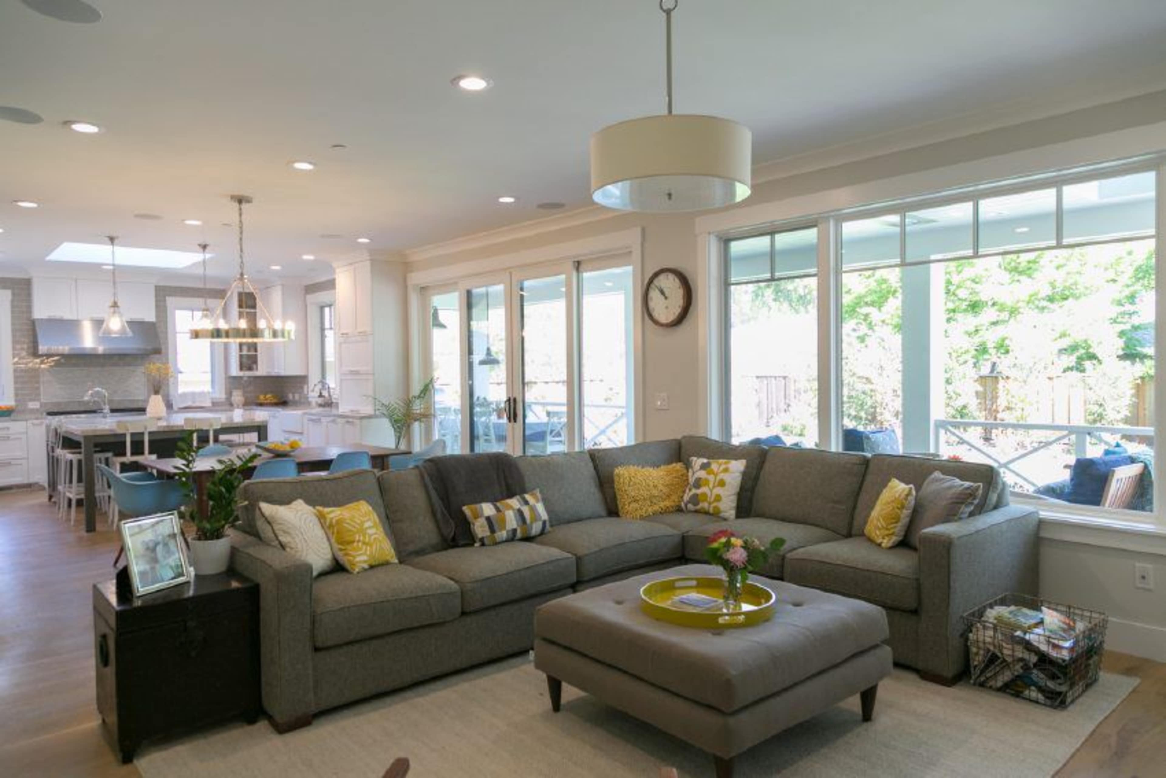 A light-filled living room featuring a large sectional sofa, a coffee table, and large windows that open to an outdoor area.