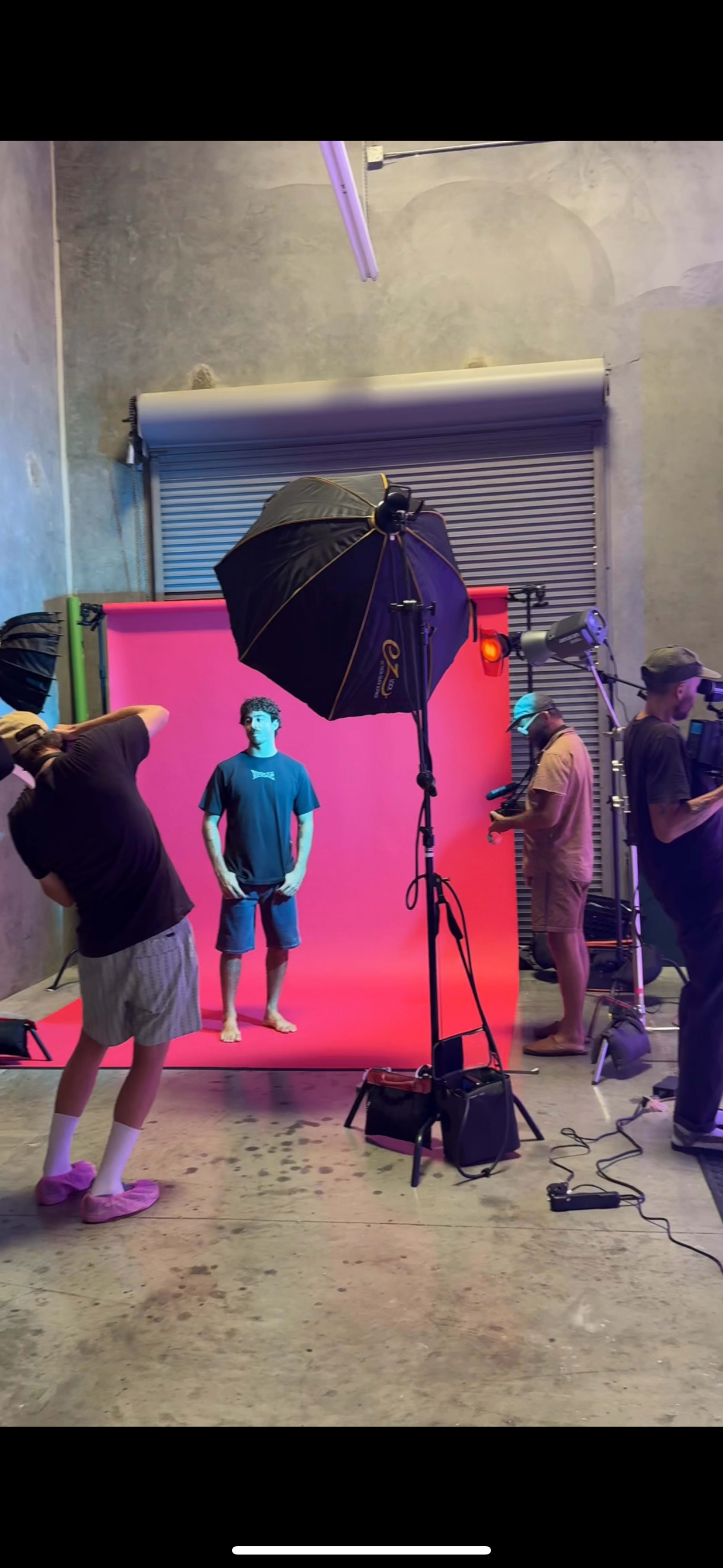 A well-lit photo shoot is taking place in a studio with a color gradient backdrop and multiple equipment setups.