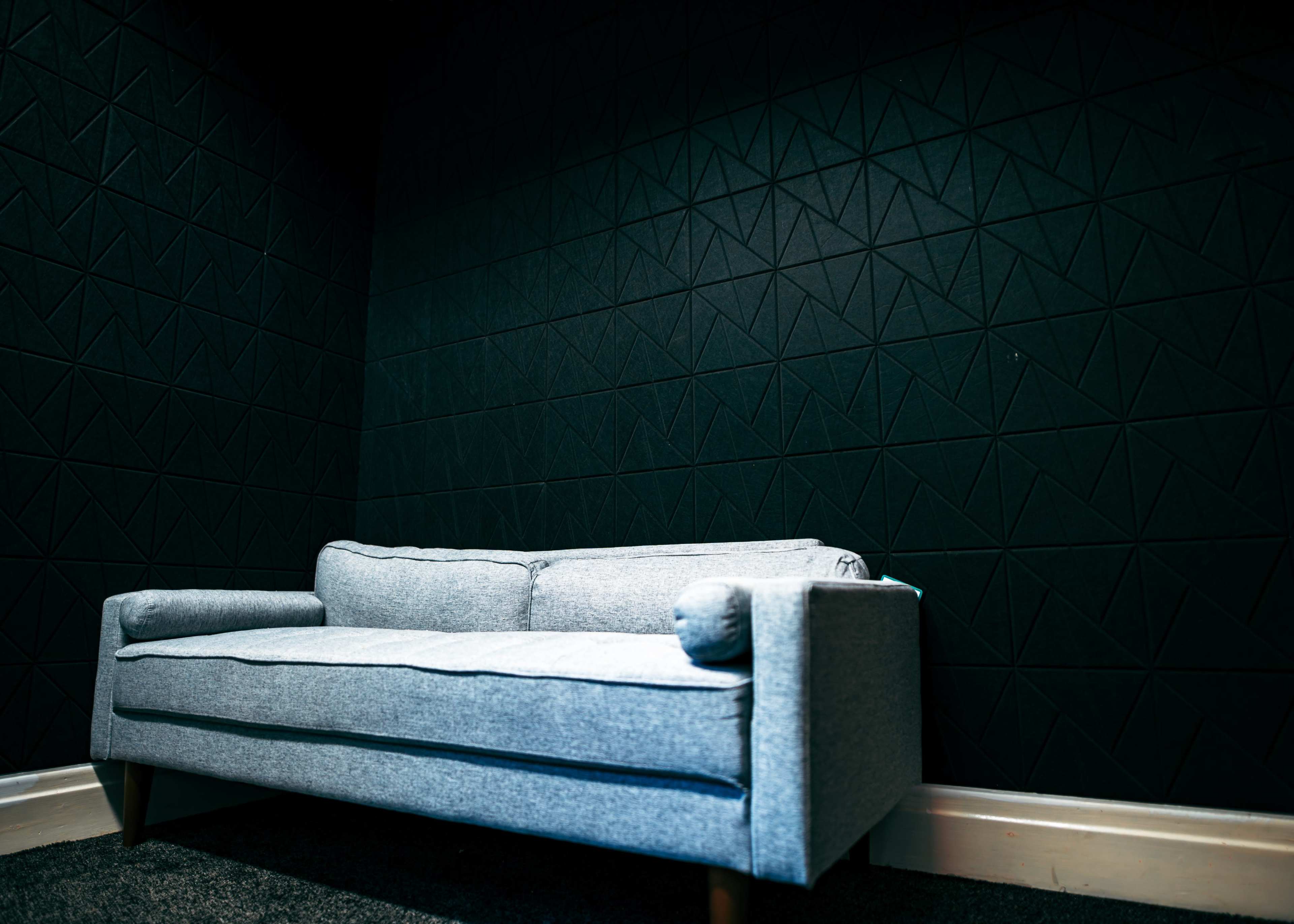 A light gray sofa with wooden legs is positioned against a dark, textured wall.