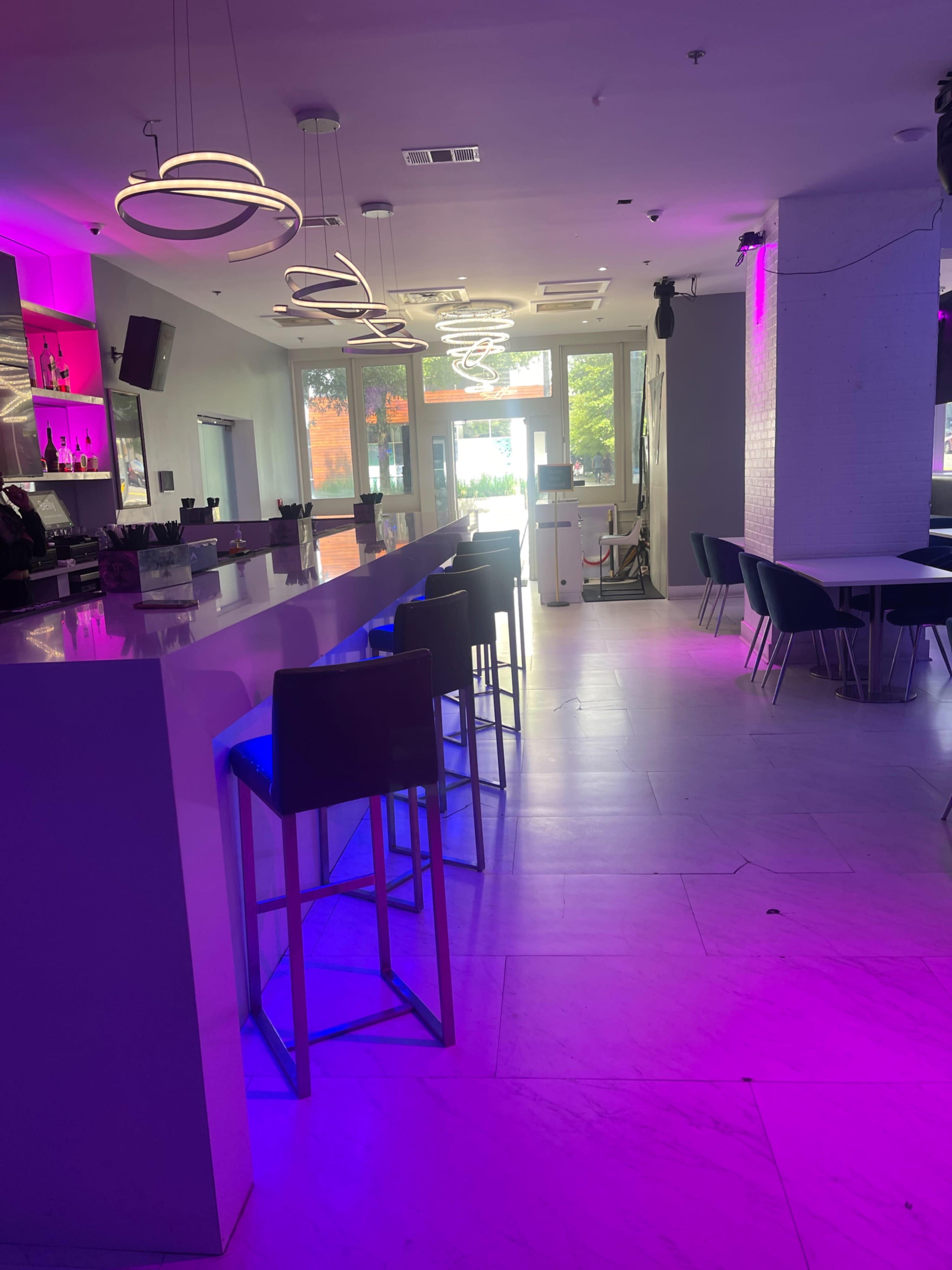 A modern bar area with a long white countertop, high stools, and purple lighting.