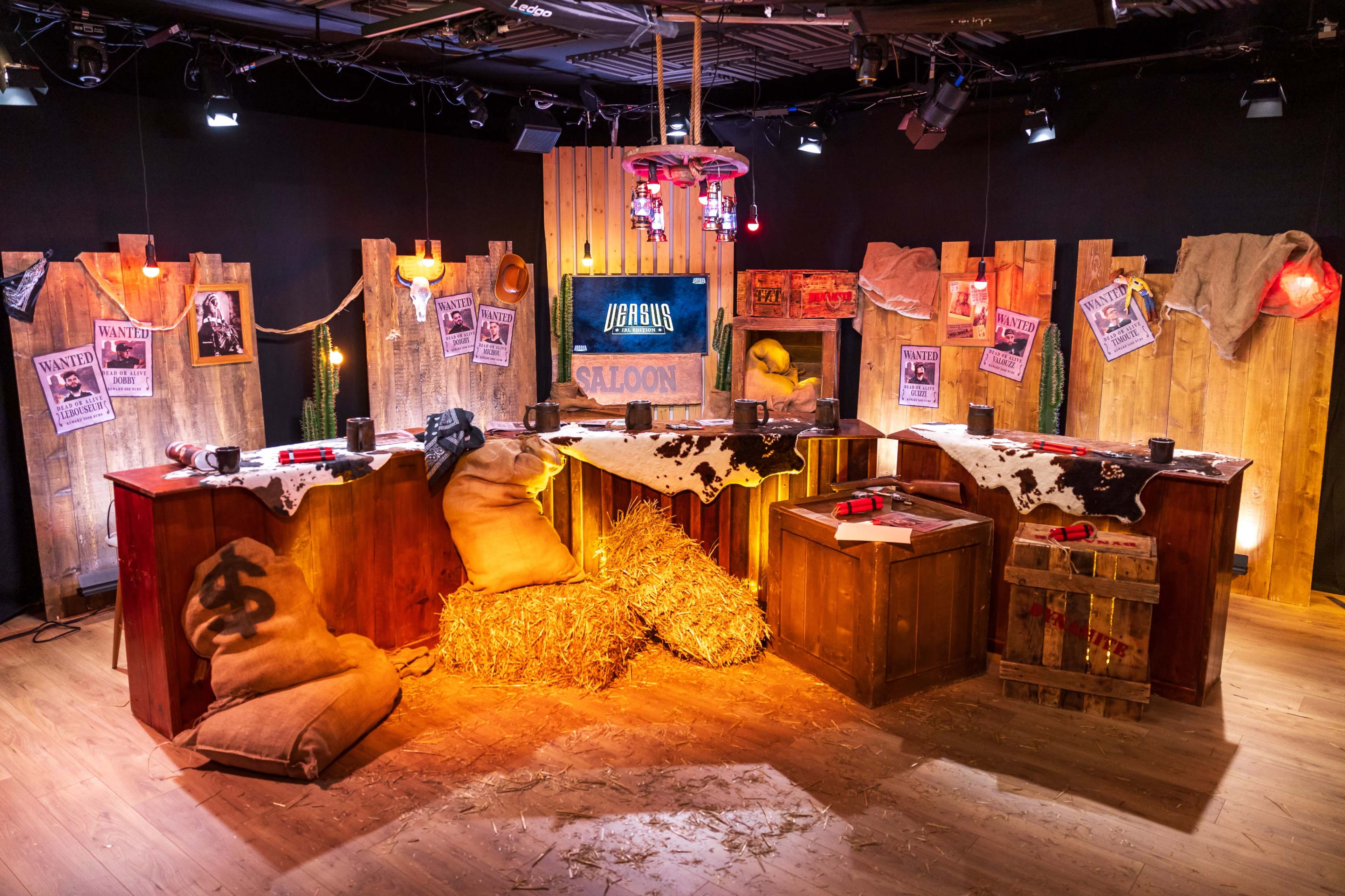A western-themed saloon set interior with wooden walls, a bar area, hay bales, and wanted posters.