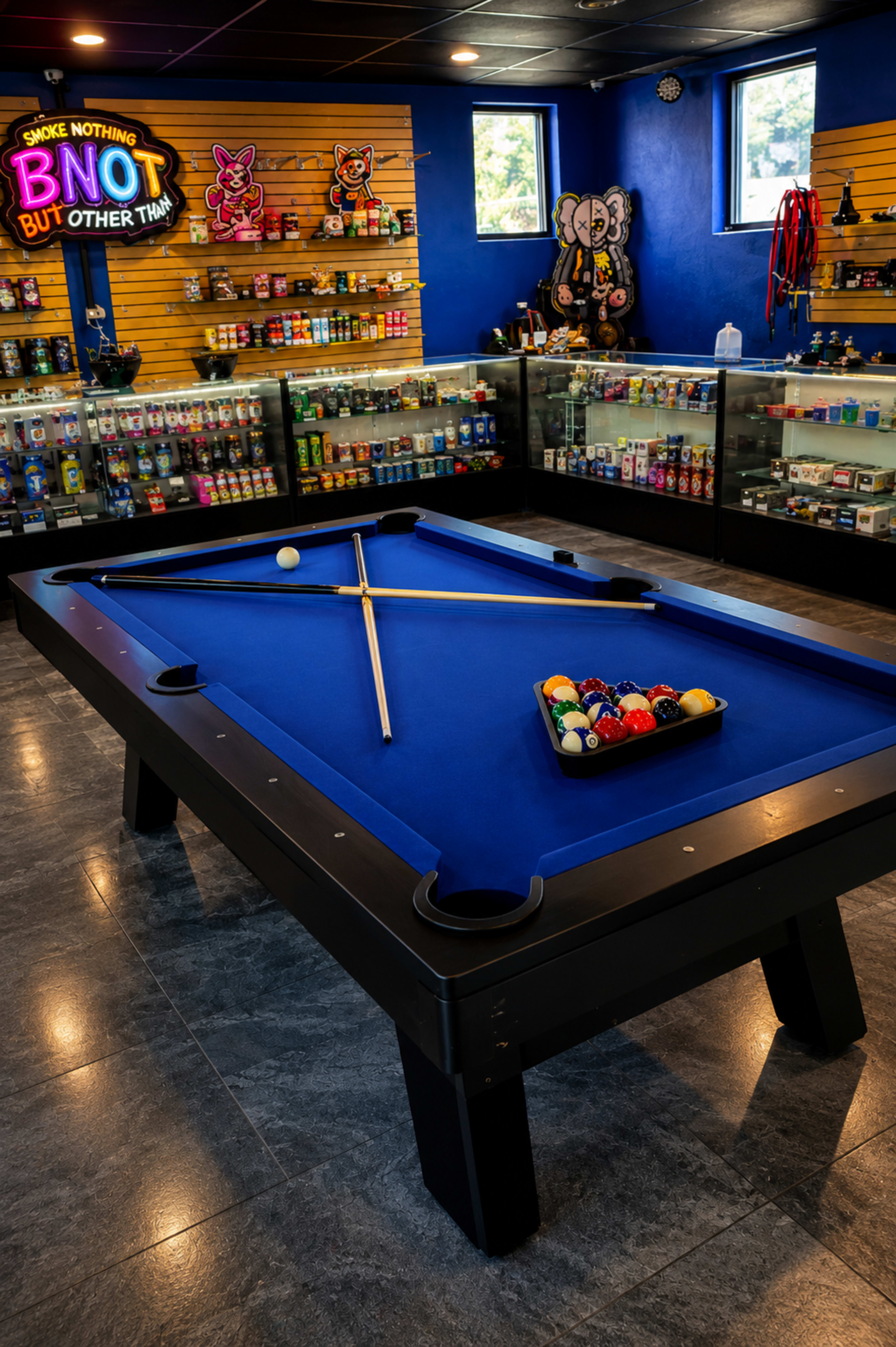 The image shows a blue felt pool table in a brightly colored game room filled with shelves of various items and a neon sign on the wall.