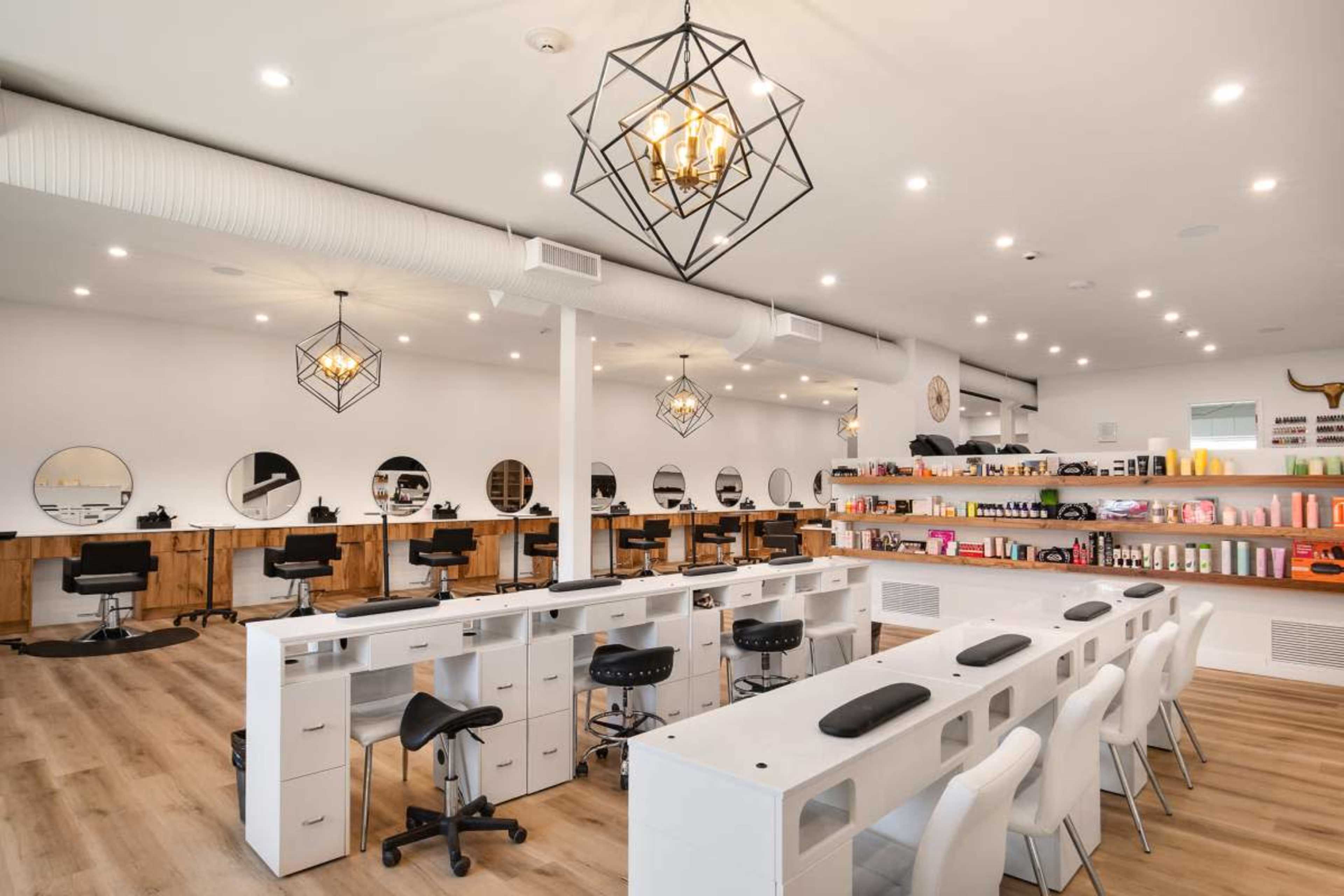 The image shows a modern salon interior with white walls, multiple styling stations featuring mirrors, black chairs, and a shelf displaying hair products.