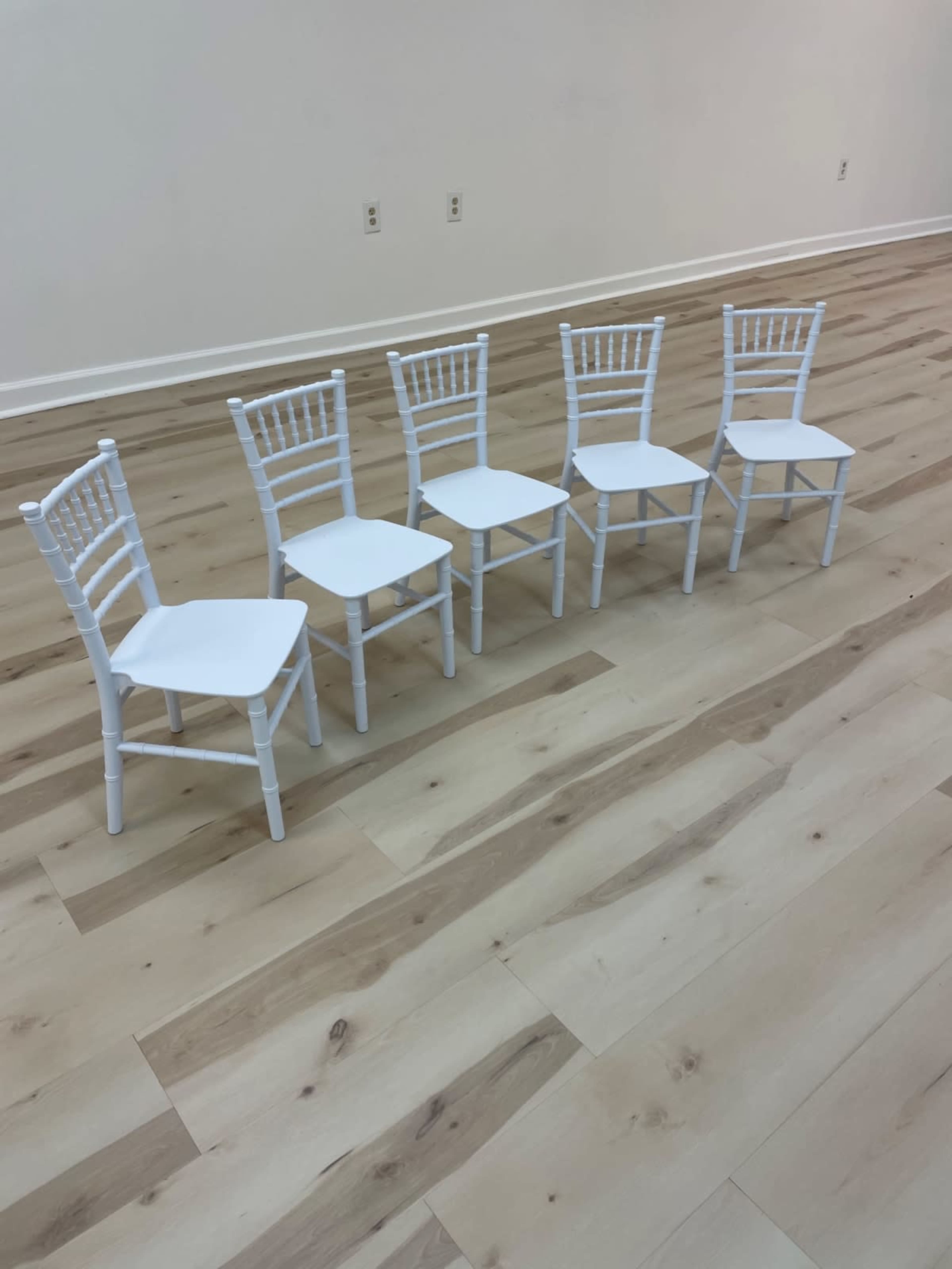 Five white chairs are arranged in a row on a light wooden floor.