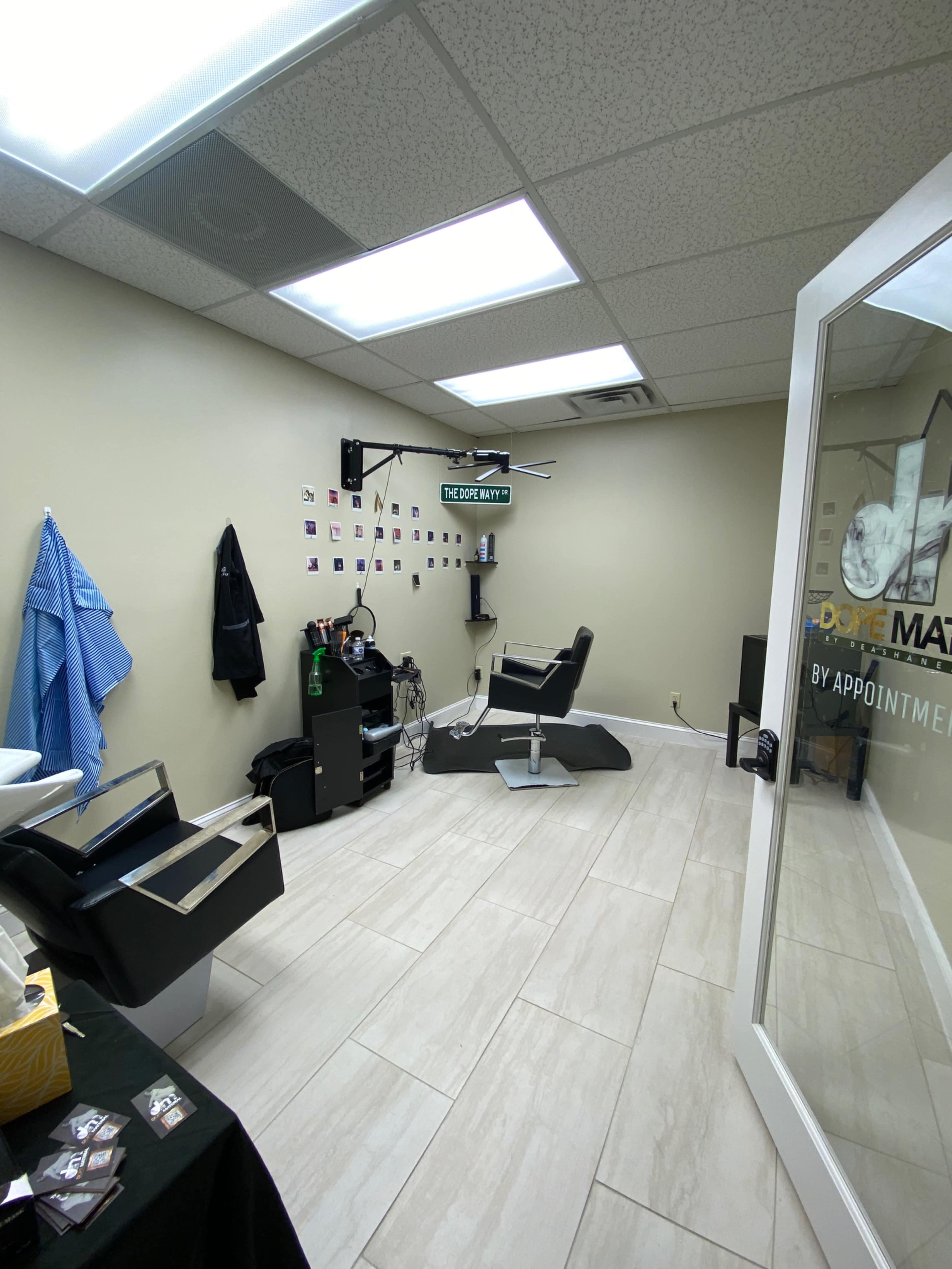 The image shows a modern barbershop interior with a styling chair, a large mirror, and a wall decorated with photographs.