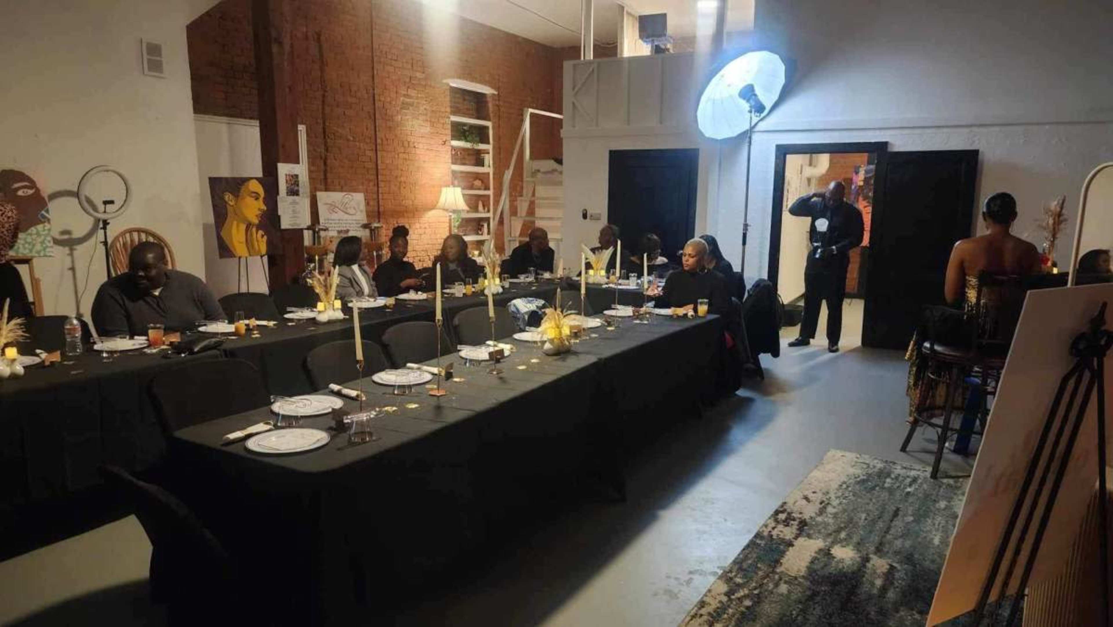 A long dining table set with plates and candles in a spacious room with artwork on the walls and people seated around the table.