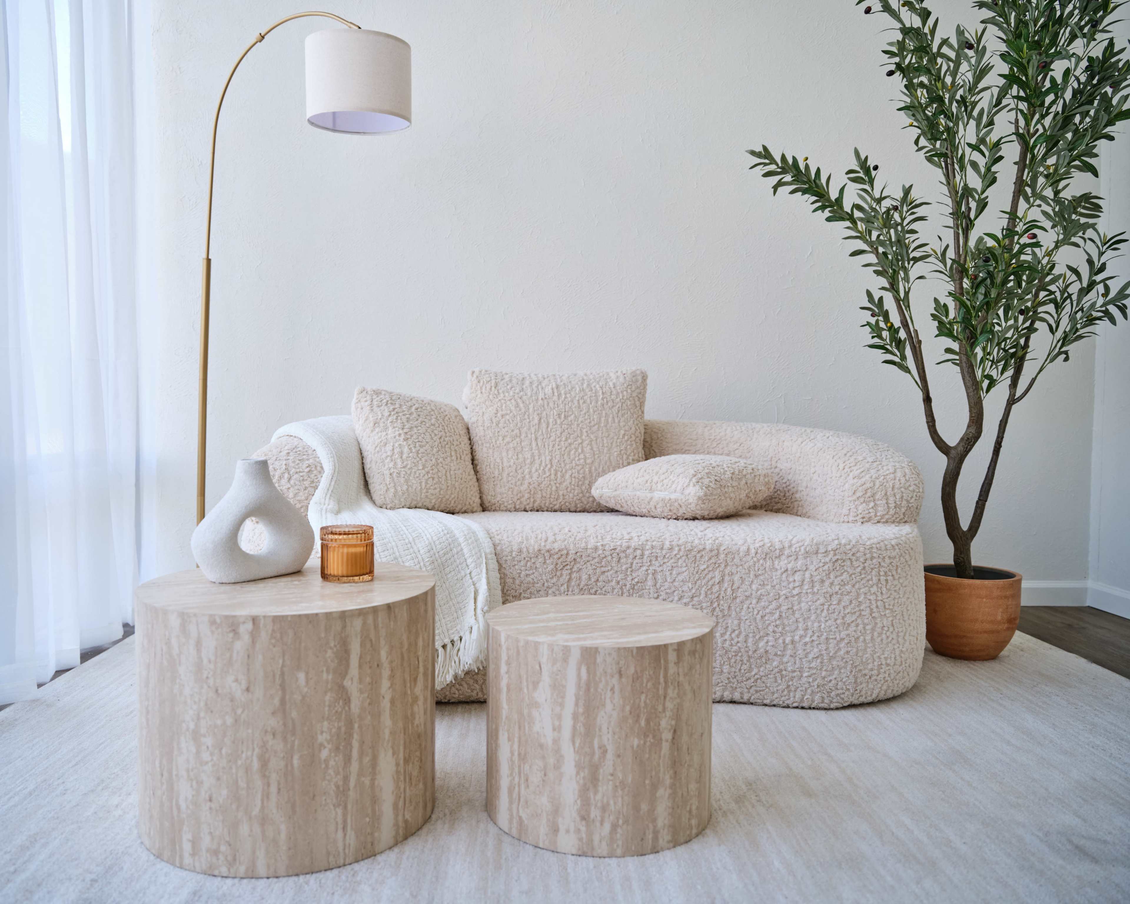 The image shows a cozy living room scene with a textured beige sofa, two round wooden coffee tables, and a potted plant in the corner.