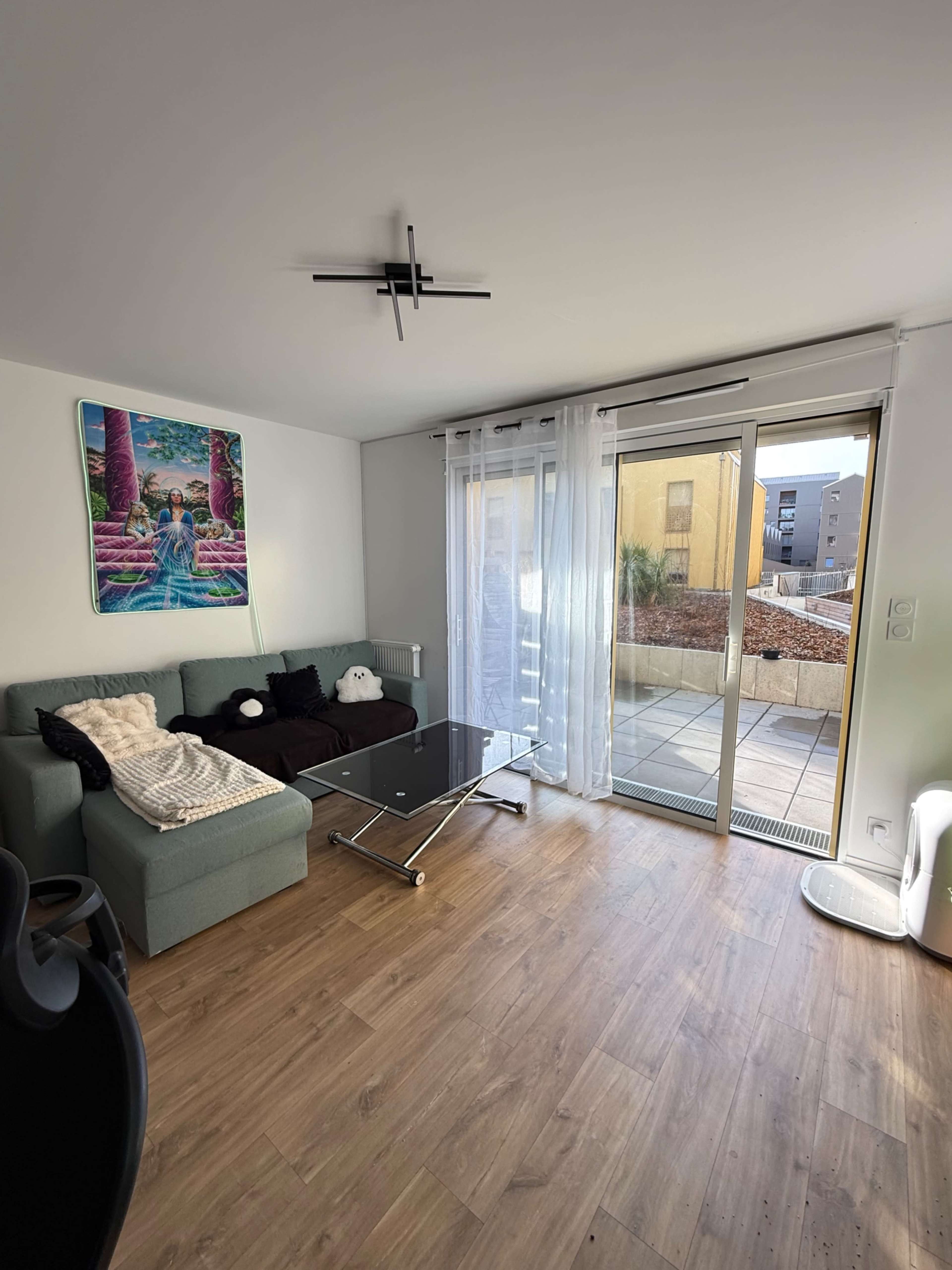 The image shows a modern living room with a light blue couch, a black glass coffee table, and a sliding glass door leading to a balcony.