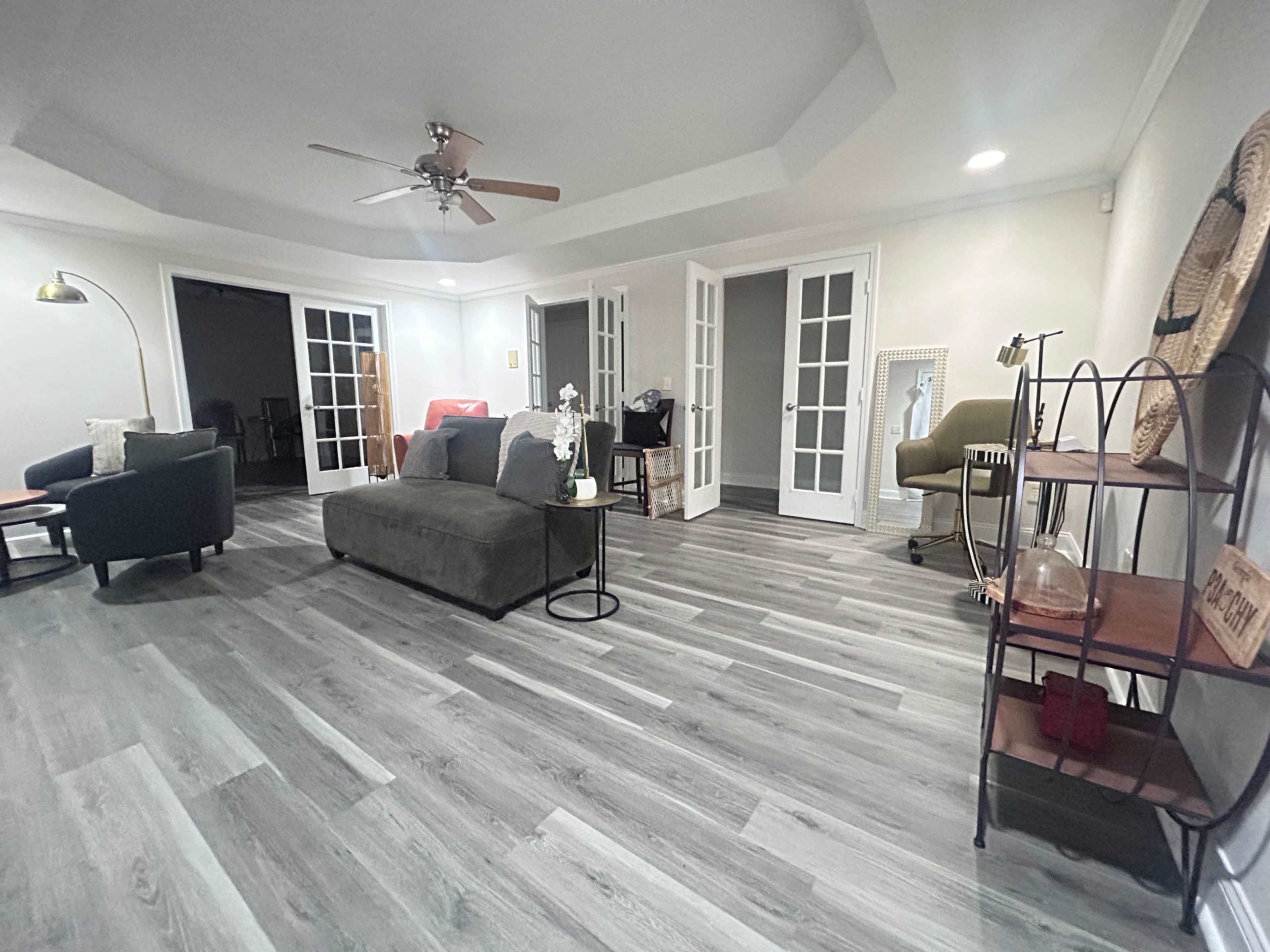 The image shows a spacious living area with a light-colored wooden floor, a few pieces of furniture, and multiple doorways leading to other rooms.