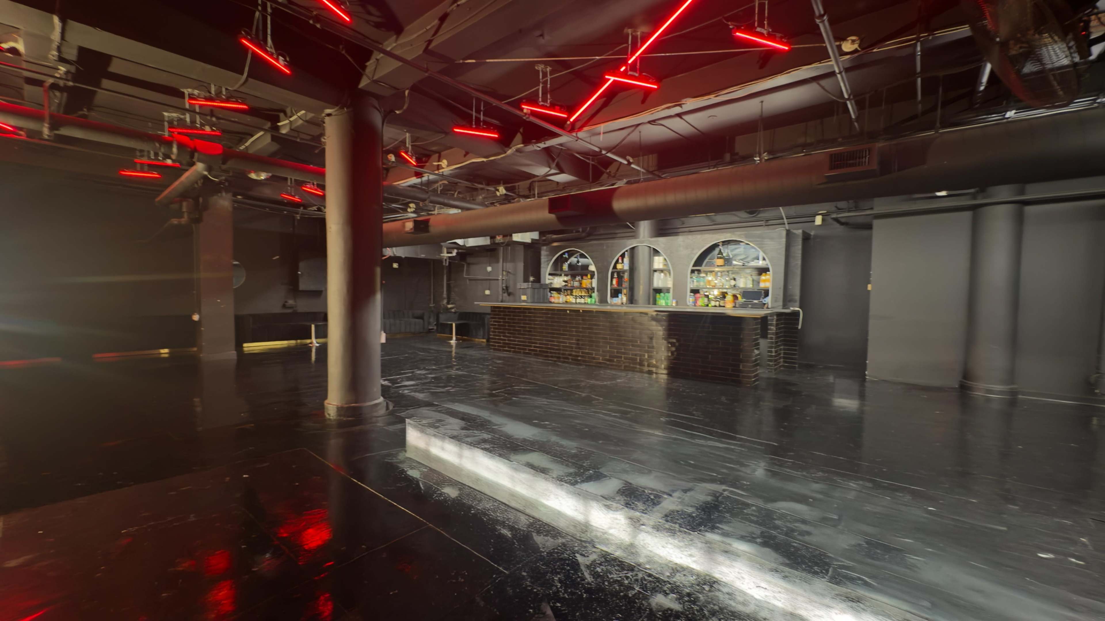 The image shows an empty nightclub interior with dark walls, a black floor, and bright red neon lights overhead.