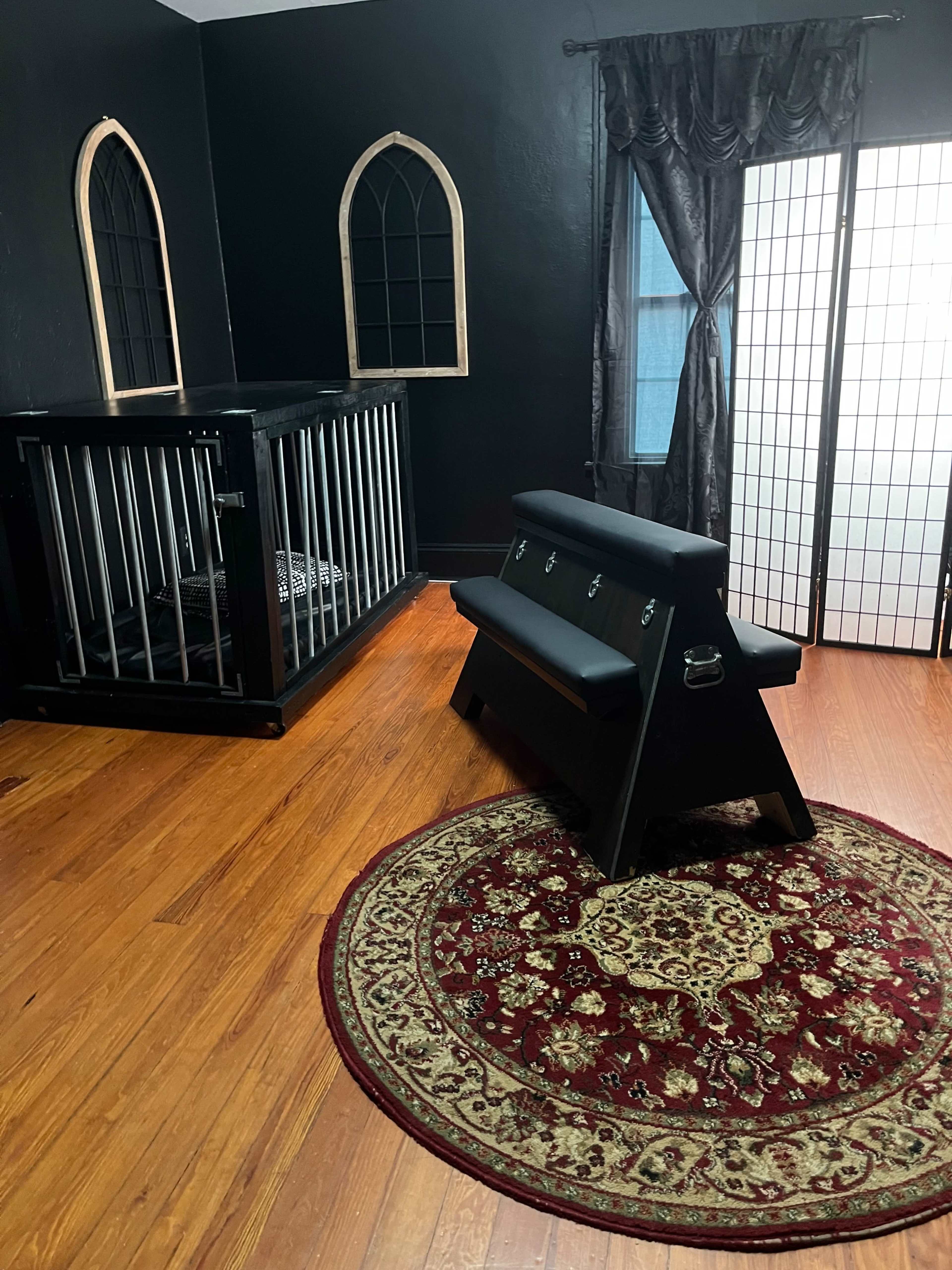 The room features dark walls, a decorative rug, a wooden bench, a caged area with bars, and a folding screen.