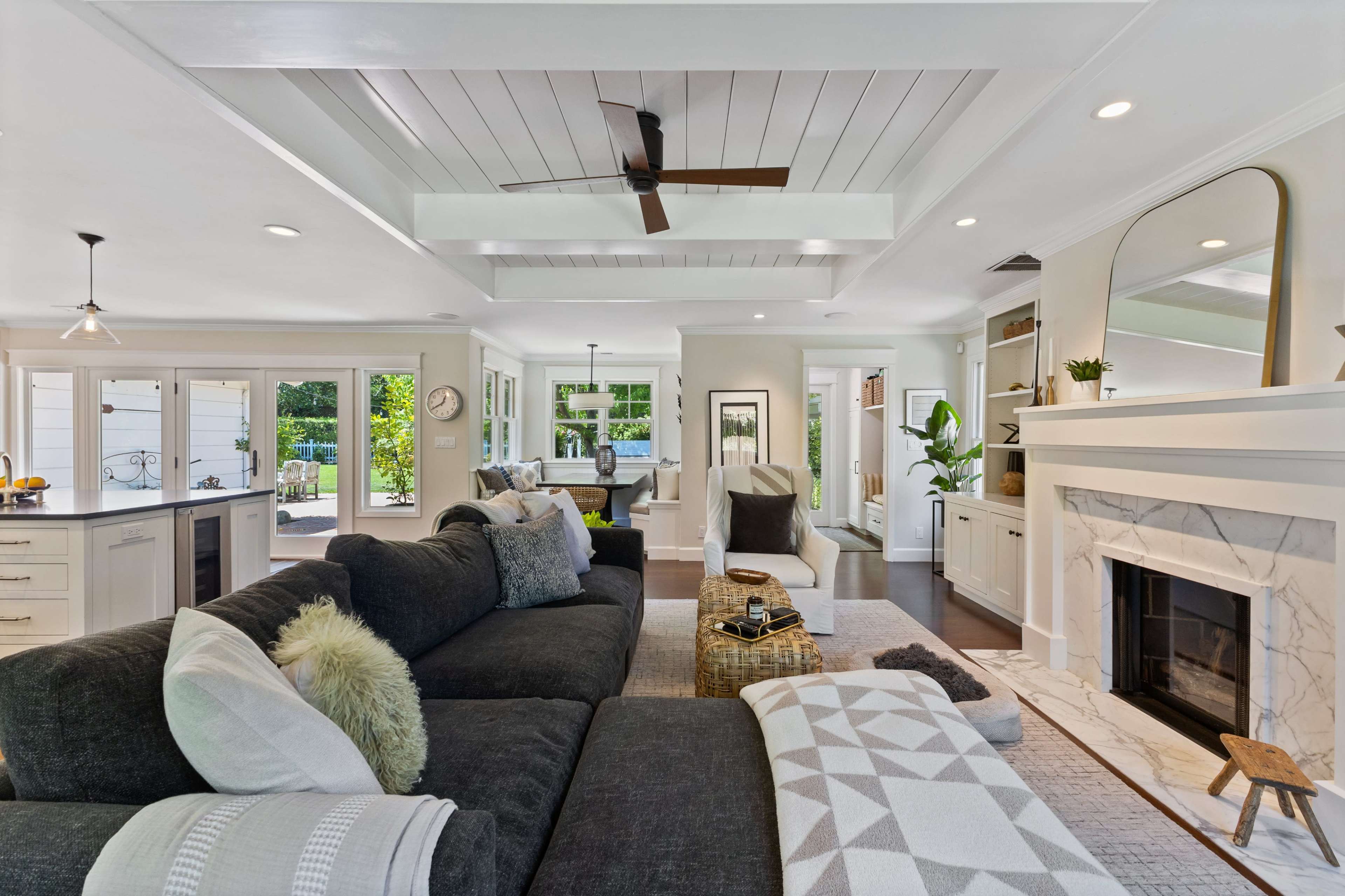 The living room features a dark sectional sofa, a marble fireplace, and large windows that offer views of the outdoors.
