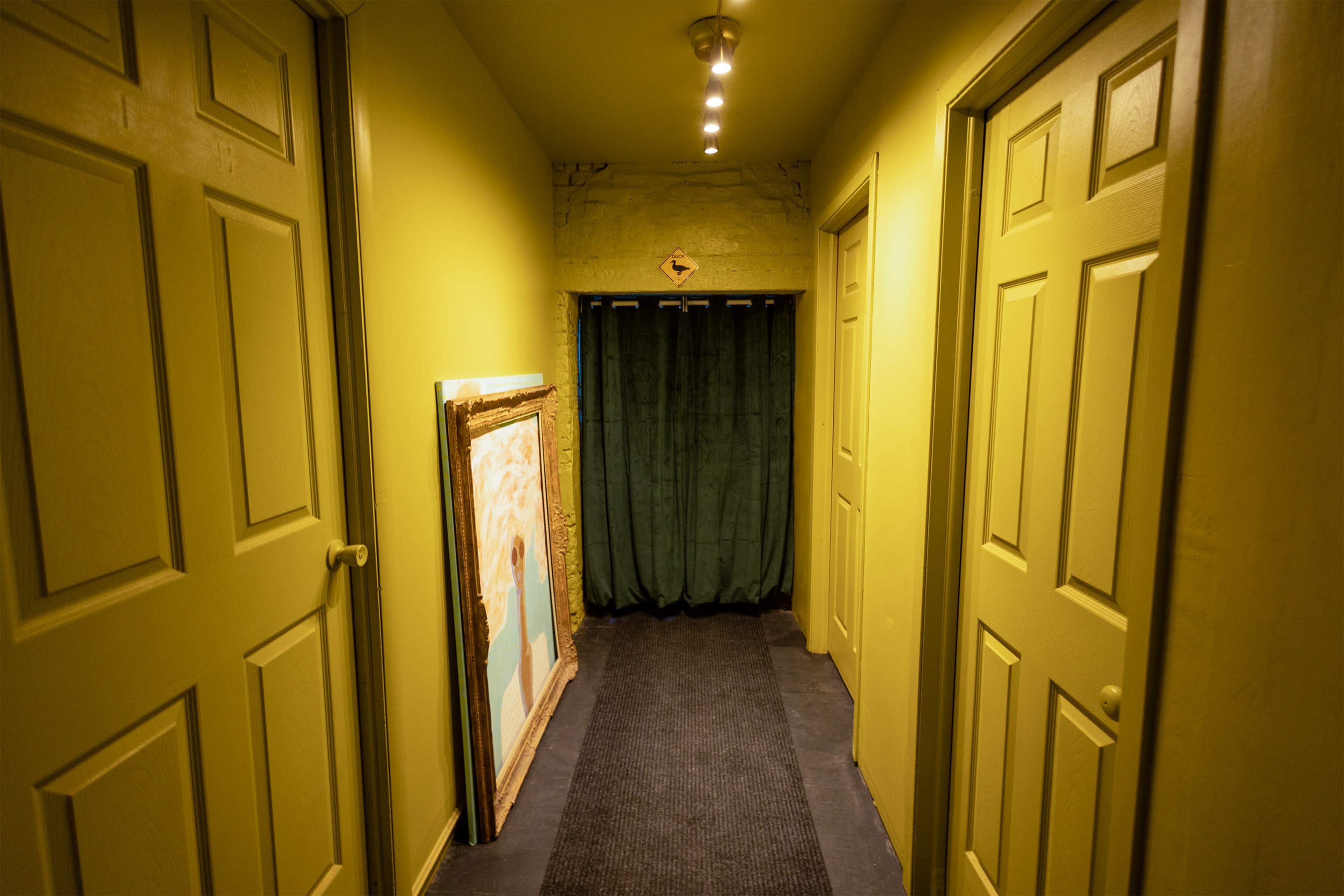A narrow hallway with green walls and doors on either side leads to a curtain at the end.