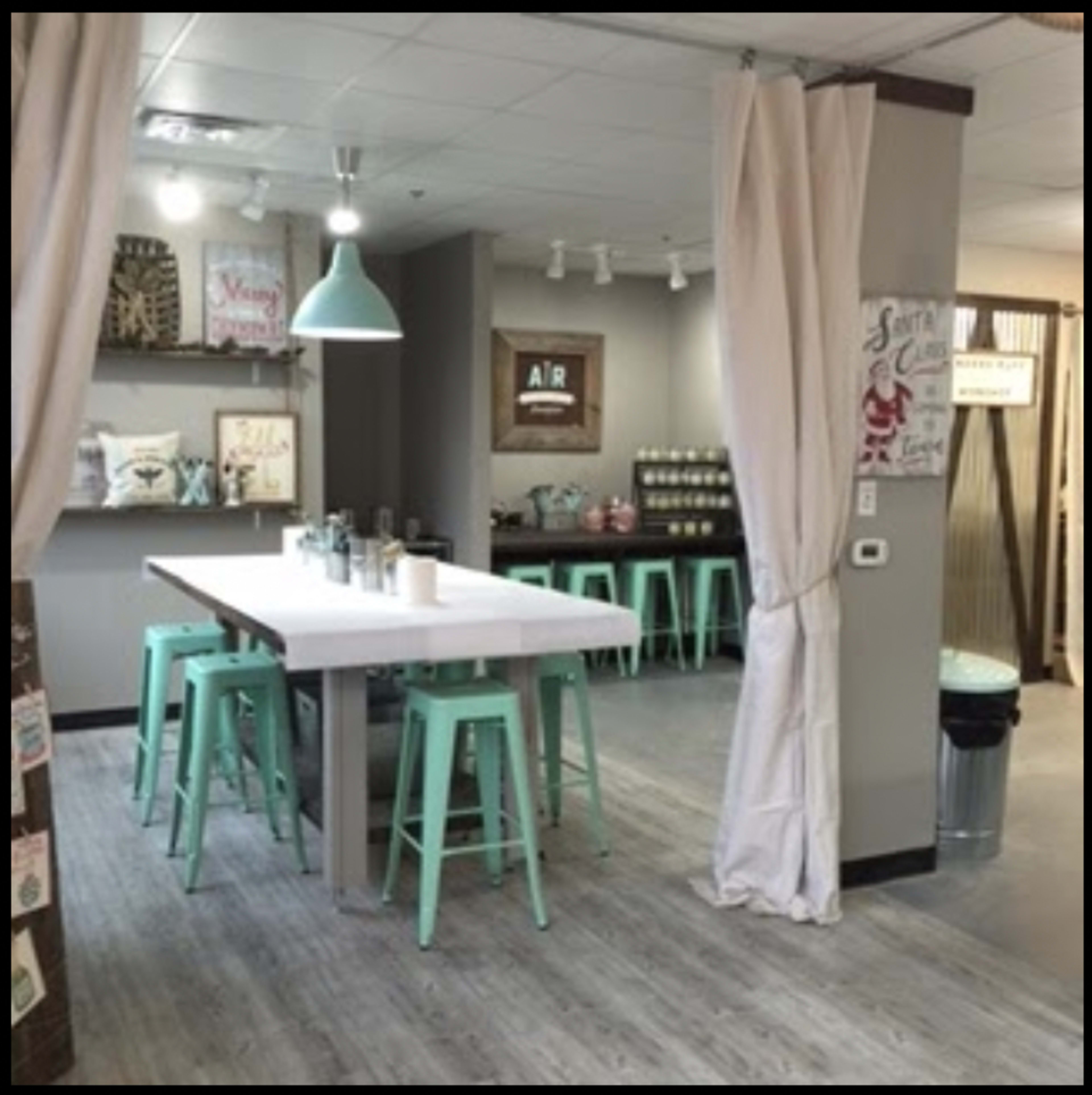 A spacious, modern kitchen area features a long white table surrounded by turquoise barstools, with a curtain partitioning the space from another room.