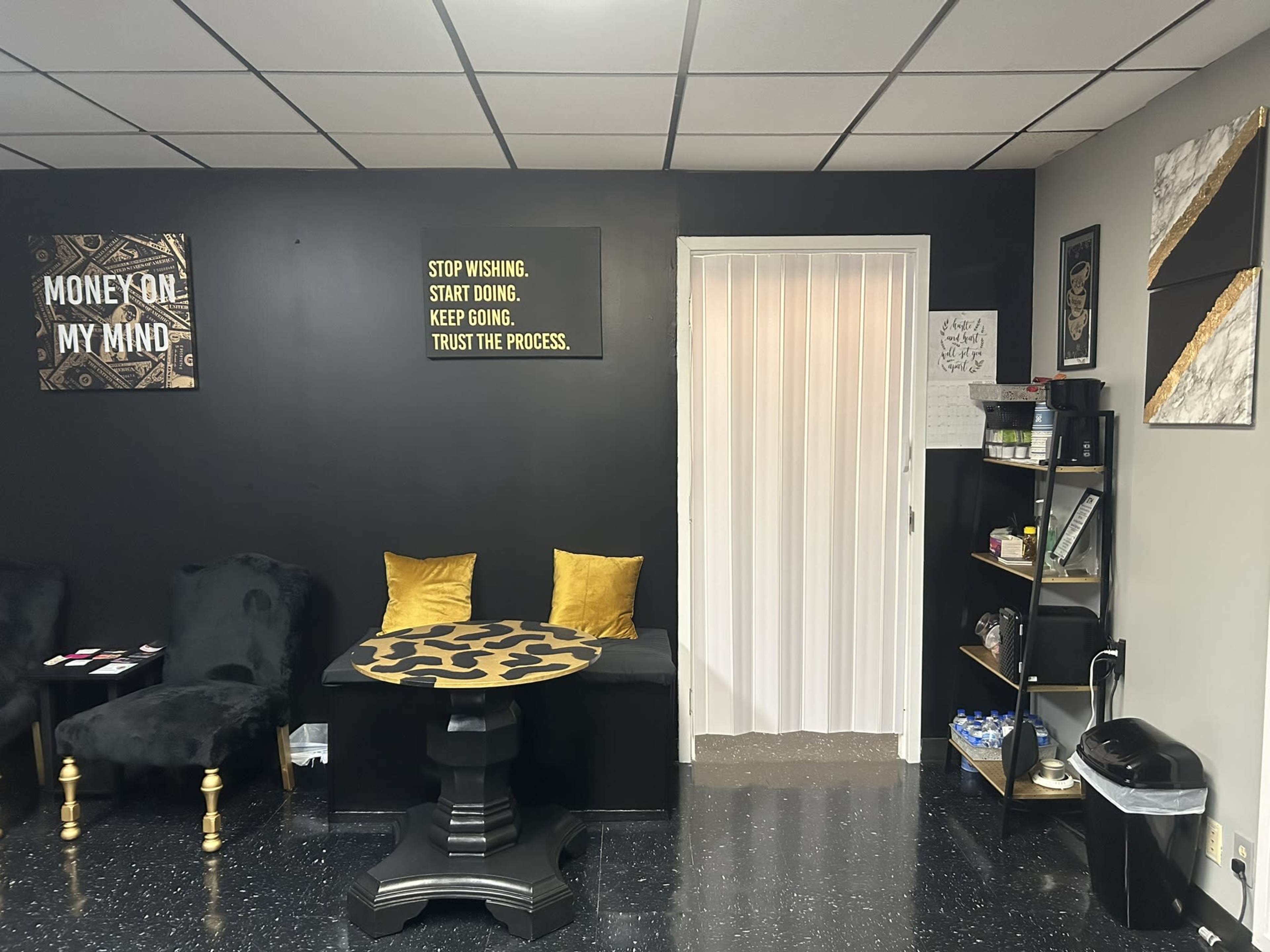 A sleek interior of a room with a dark wall, a table with a leopard-print design, two yellow cushions on chairs, and a bookshelf filled with various items.