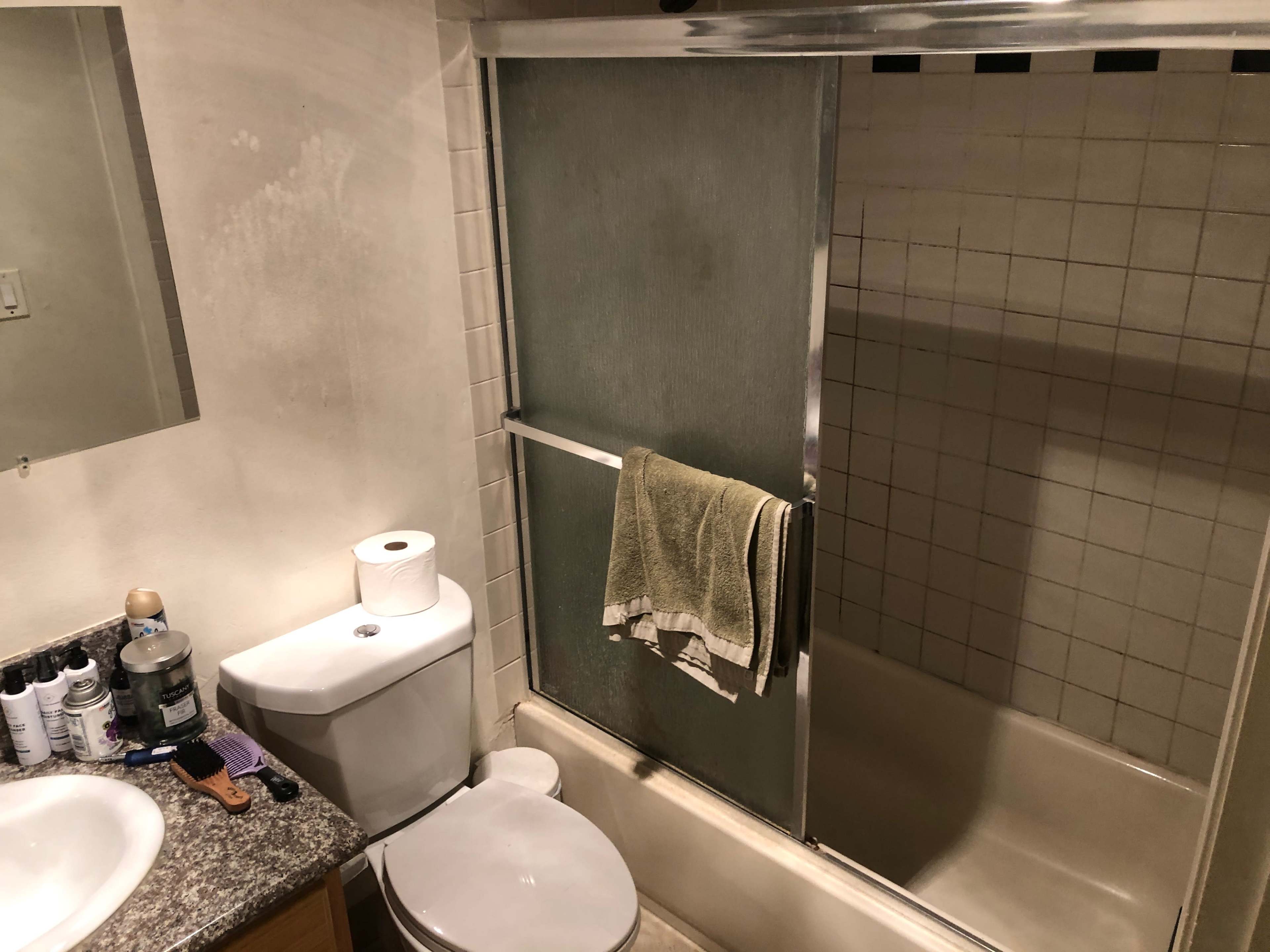 A bathroom features a shower with sliding glass doors, a toilet, and a sink with toiletries on the counter.