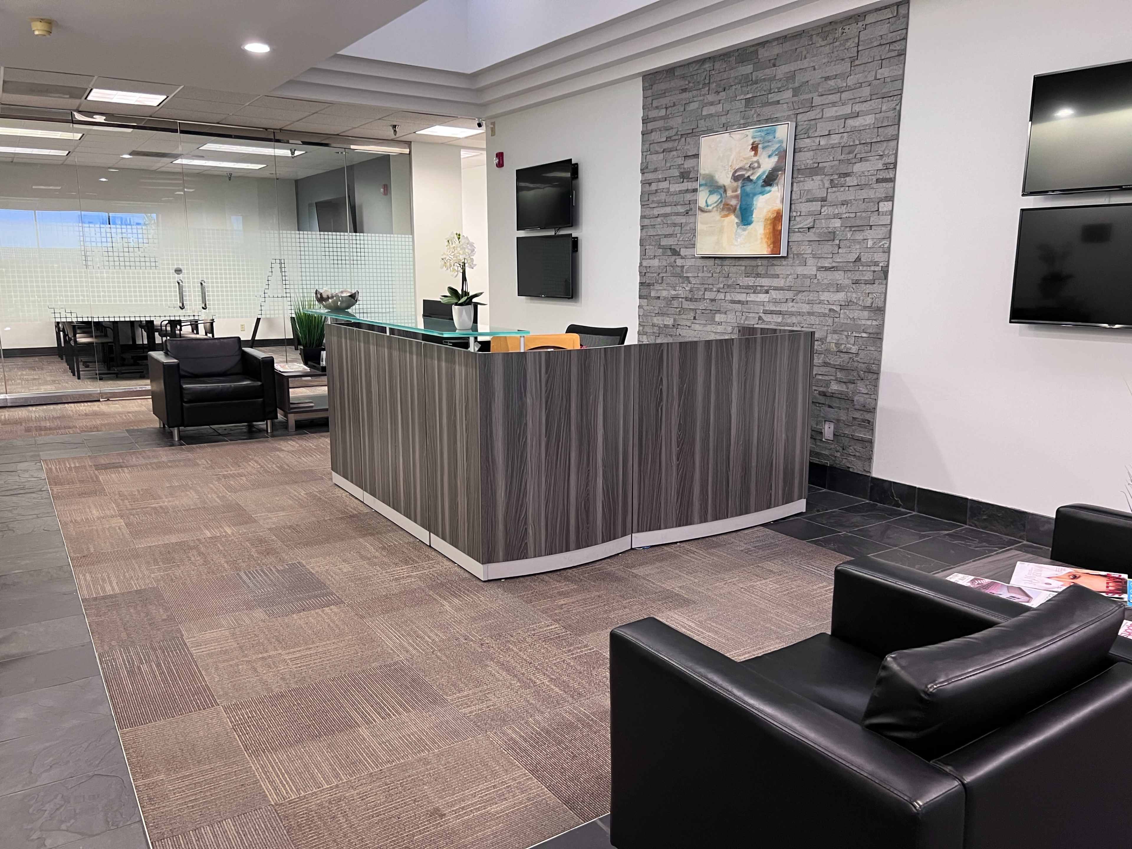 A modern reception area with a stone feature wall, a wooden front desk, and black chairs.