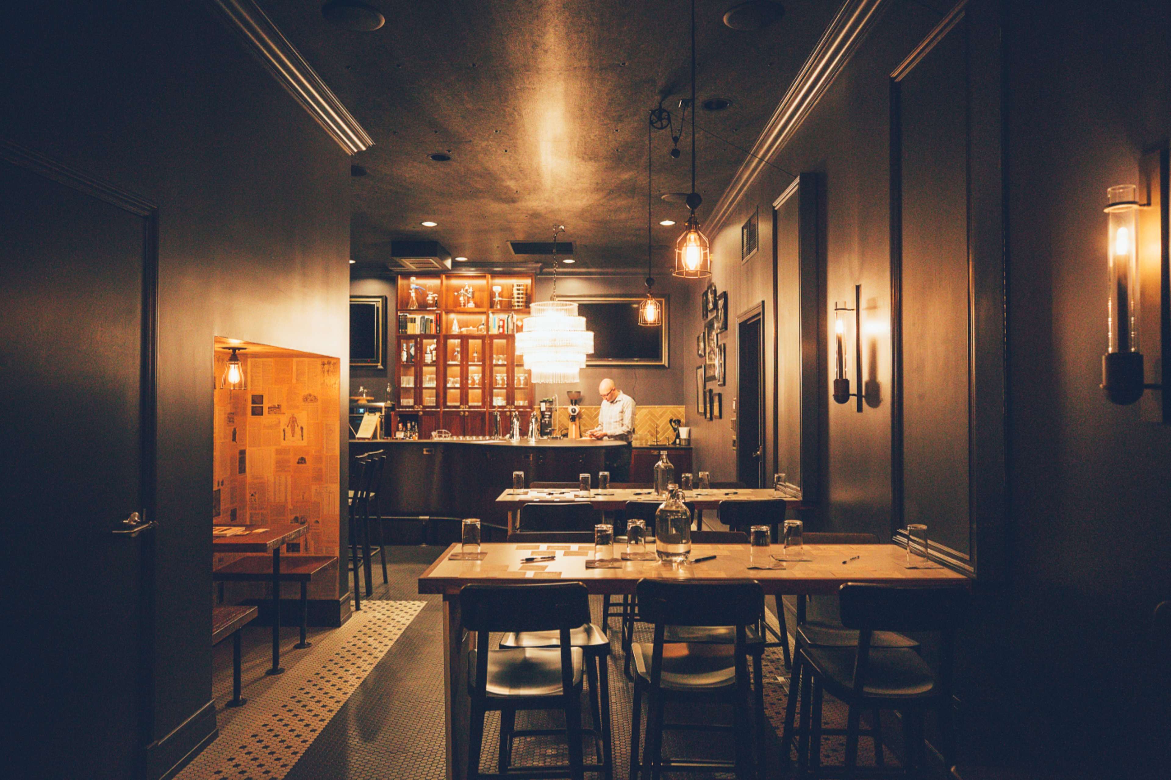 A dimly lit restaurant interior features a bar with wooden shelves and a table setup for dining.