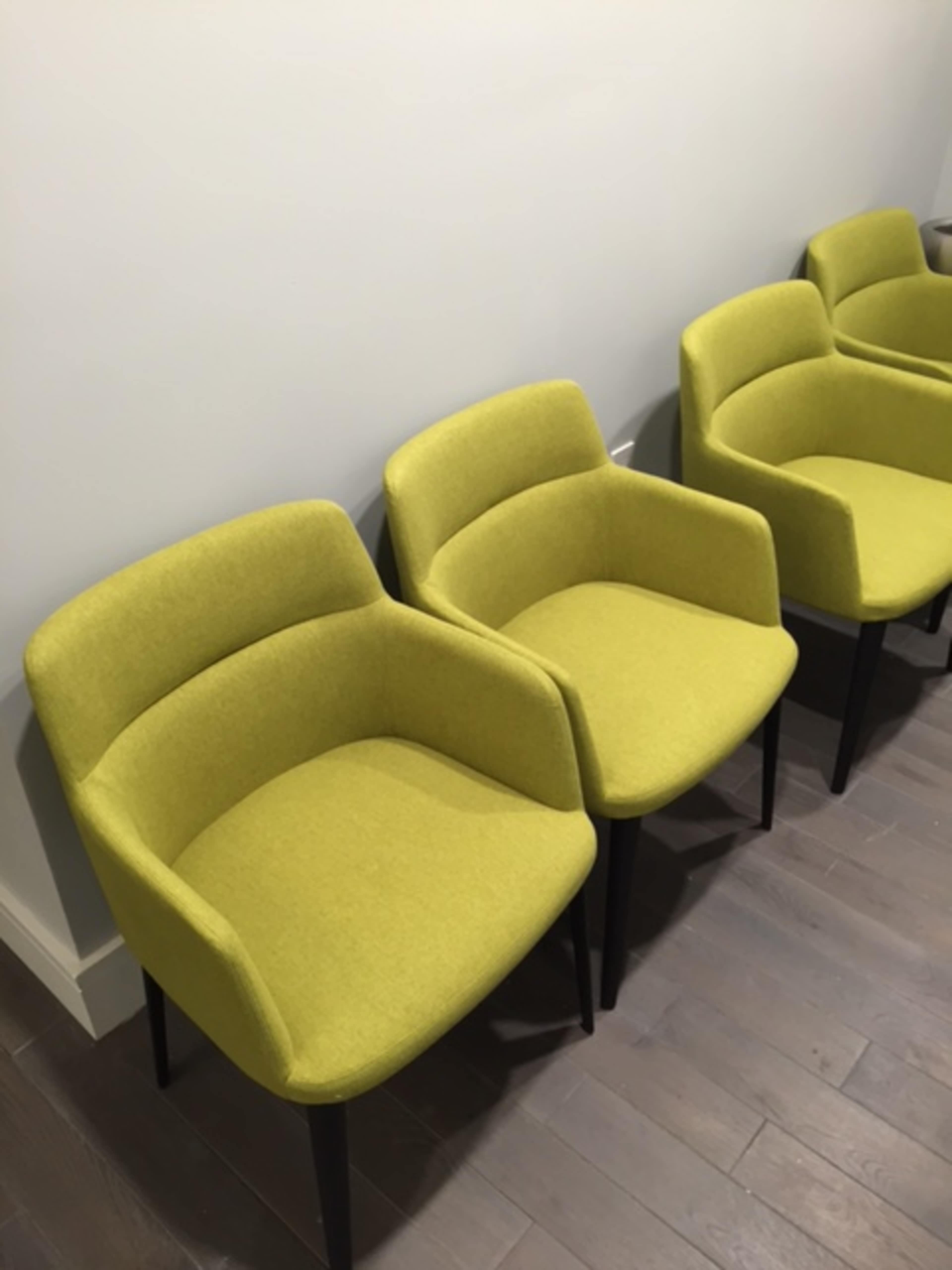 A row of four green upholstered chairs with armrests on a wooden floor.