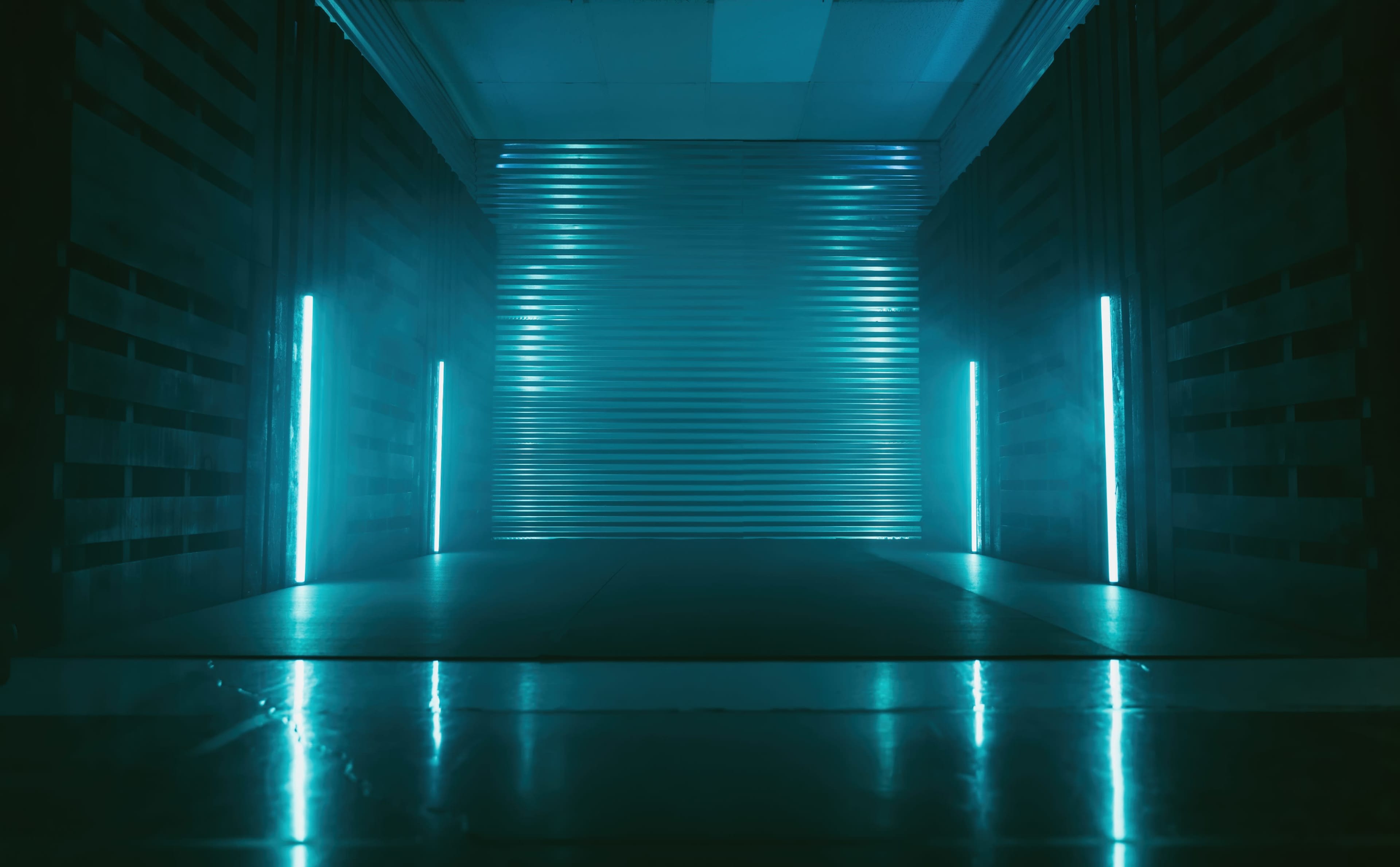 A dimly lit corridor with glowing blue lights along the walls and a metallic corrugated backdrop.