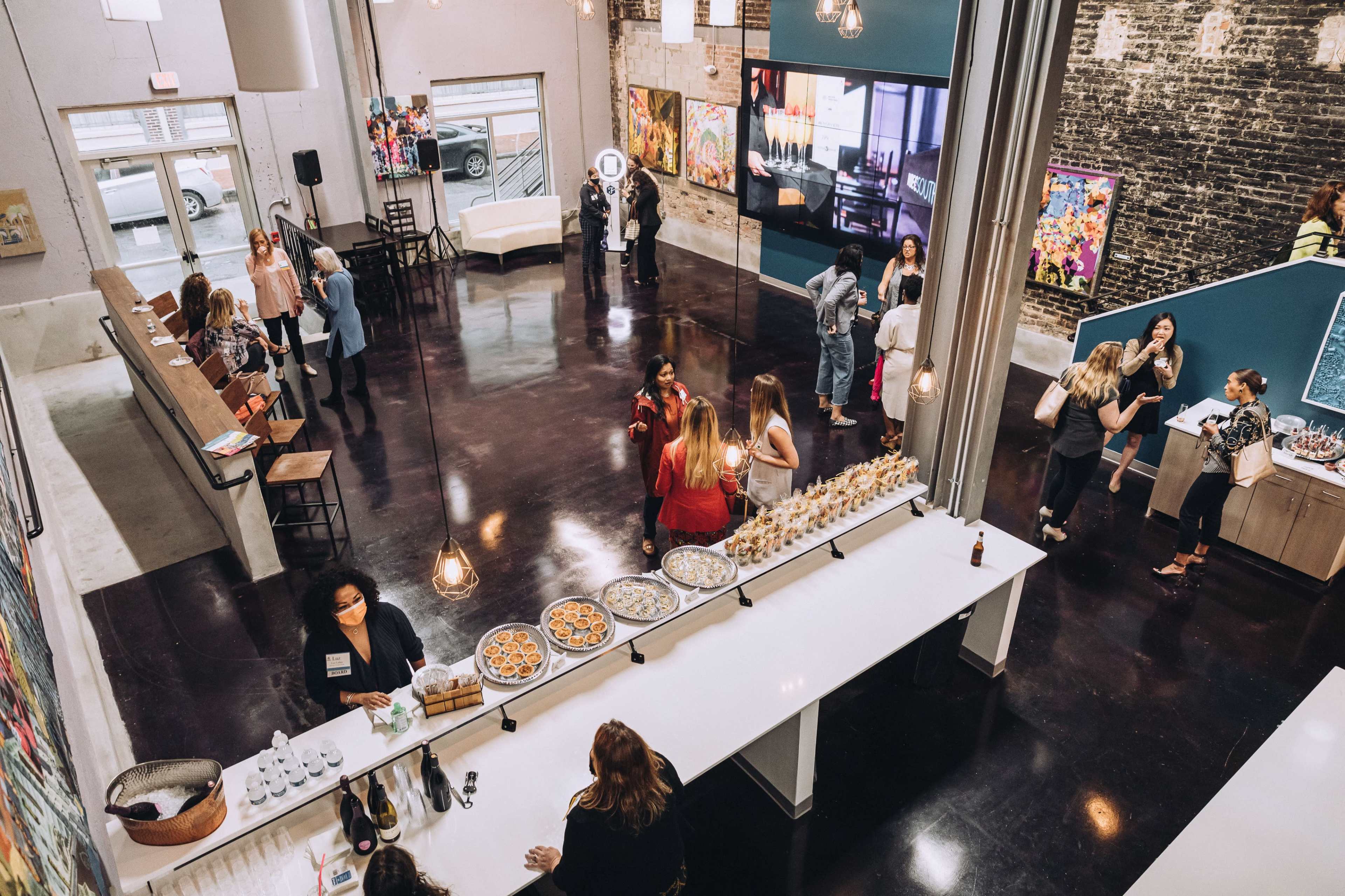 A modern event space with a long white bar, people mingling, and artwork displayed on the walls.