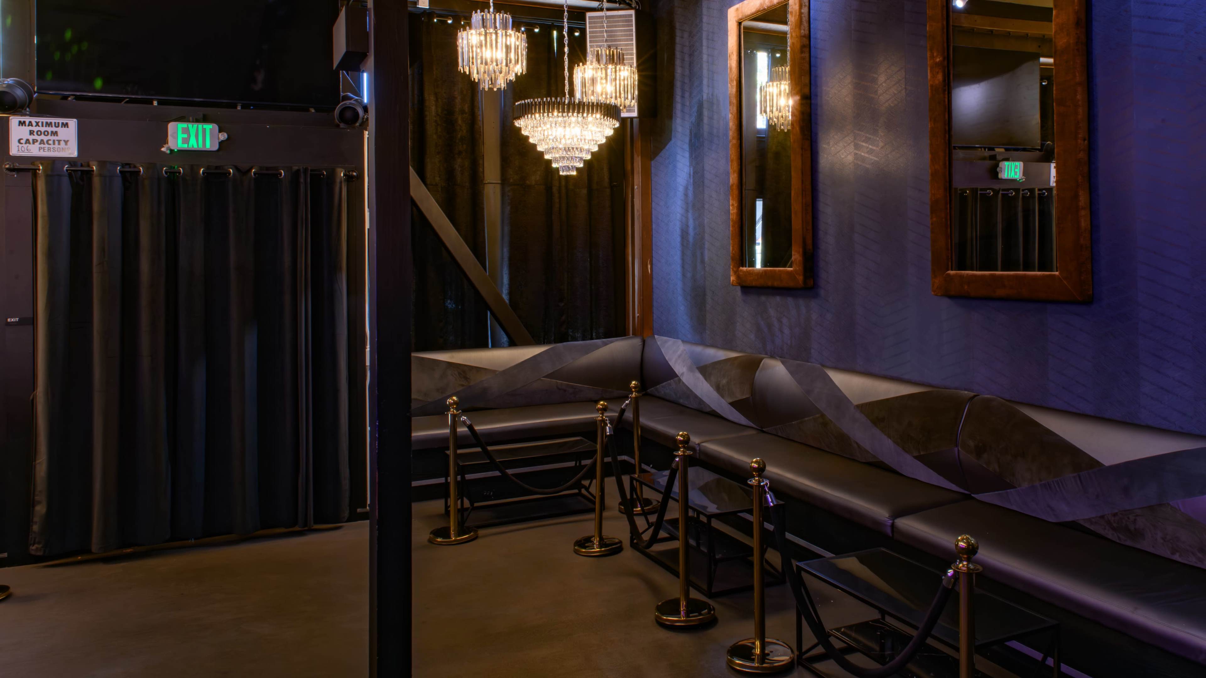The image shows an upscale lounge area with black seating, chandeliers, and mirrors, separated by velvet ropes.