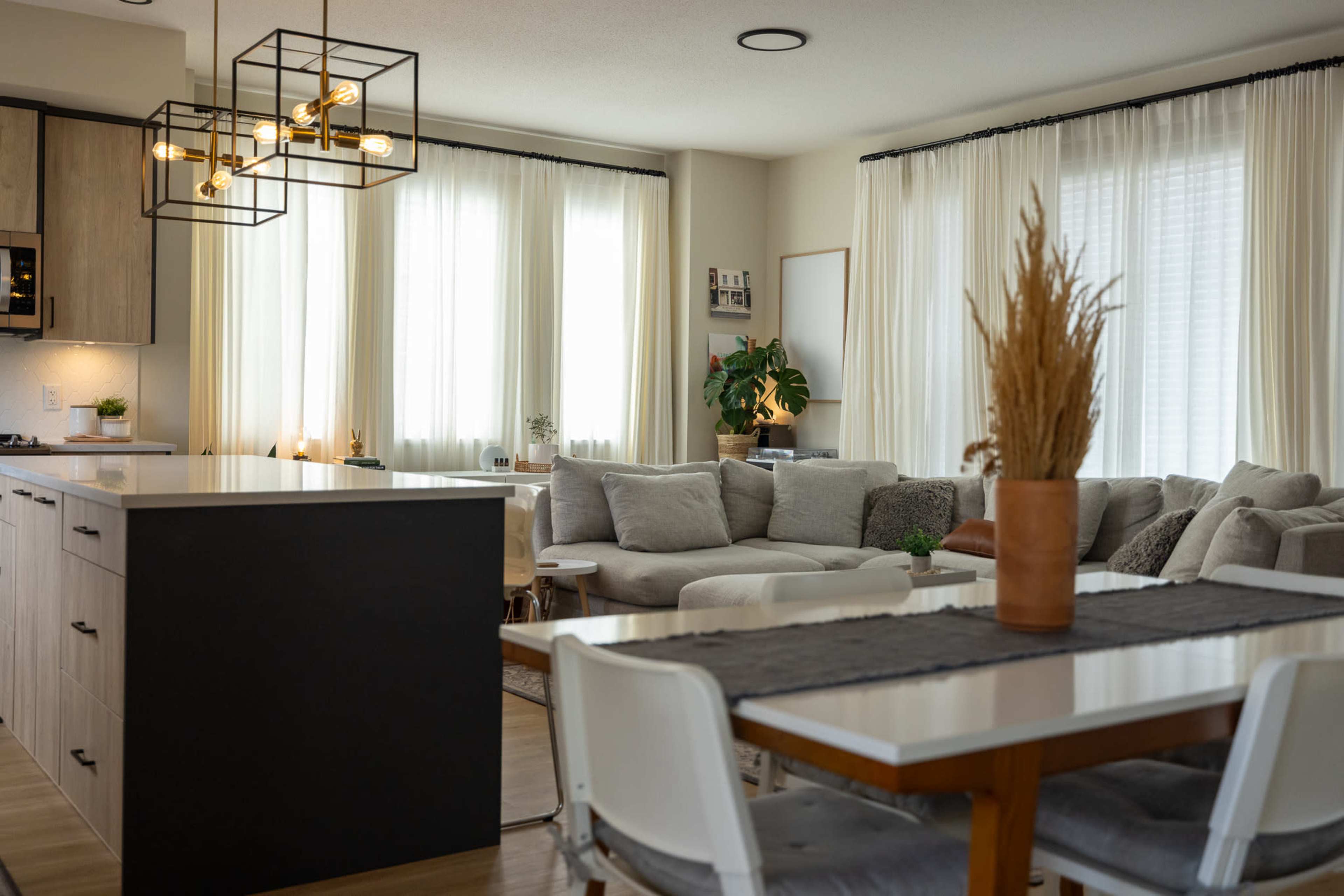 A modern open living space with a kitchen, dining area, and a comfortable seating area featuring large windows and light-colored furnishings.