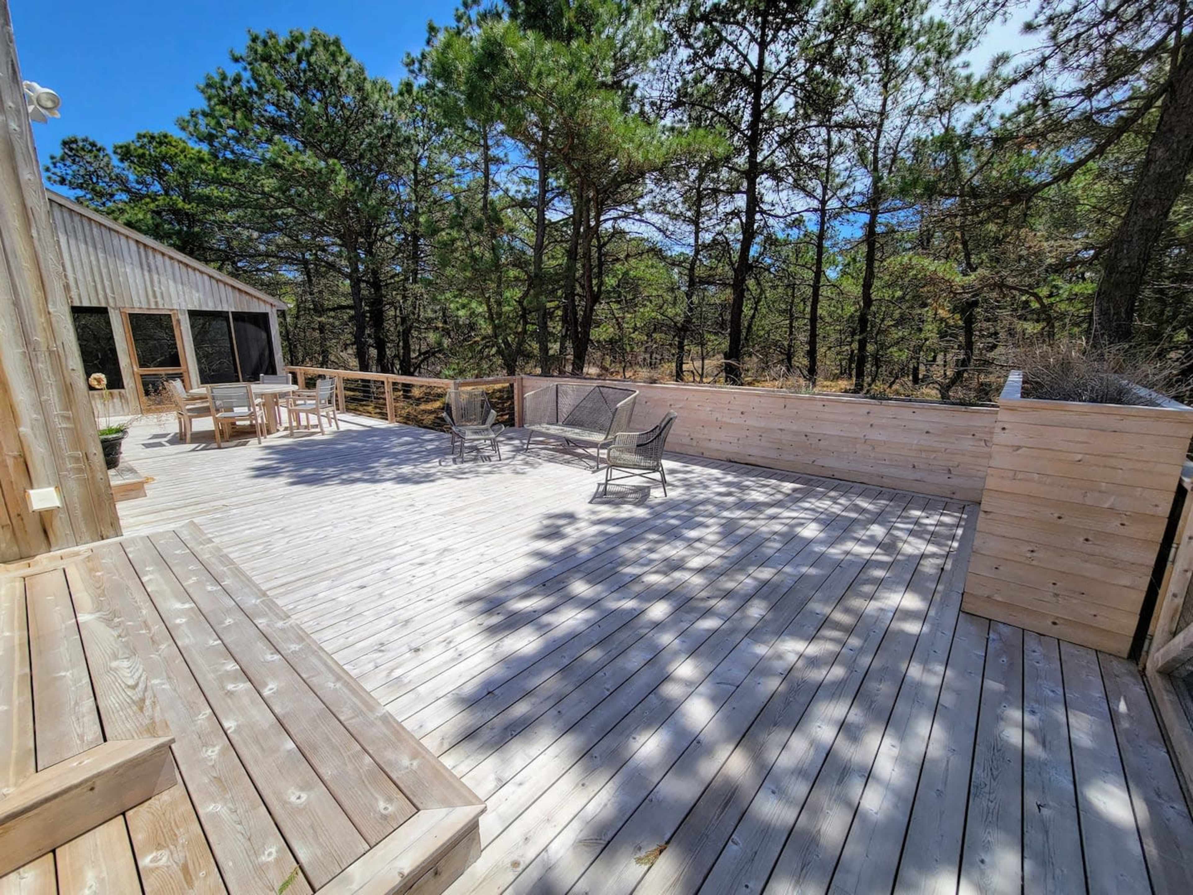 A wooden deck surrounded by trees features a few chairs and tables, creating an outdoor seating area.