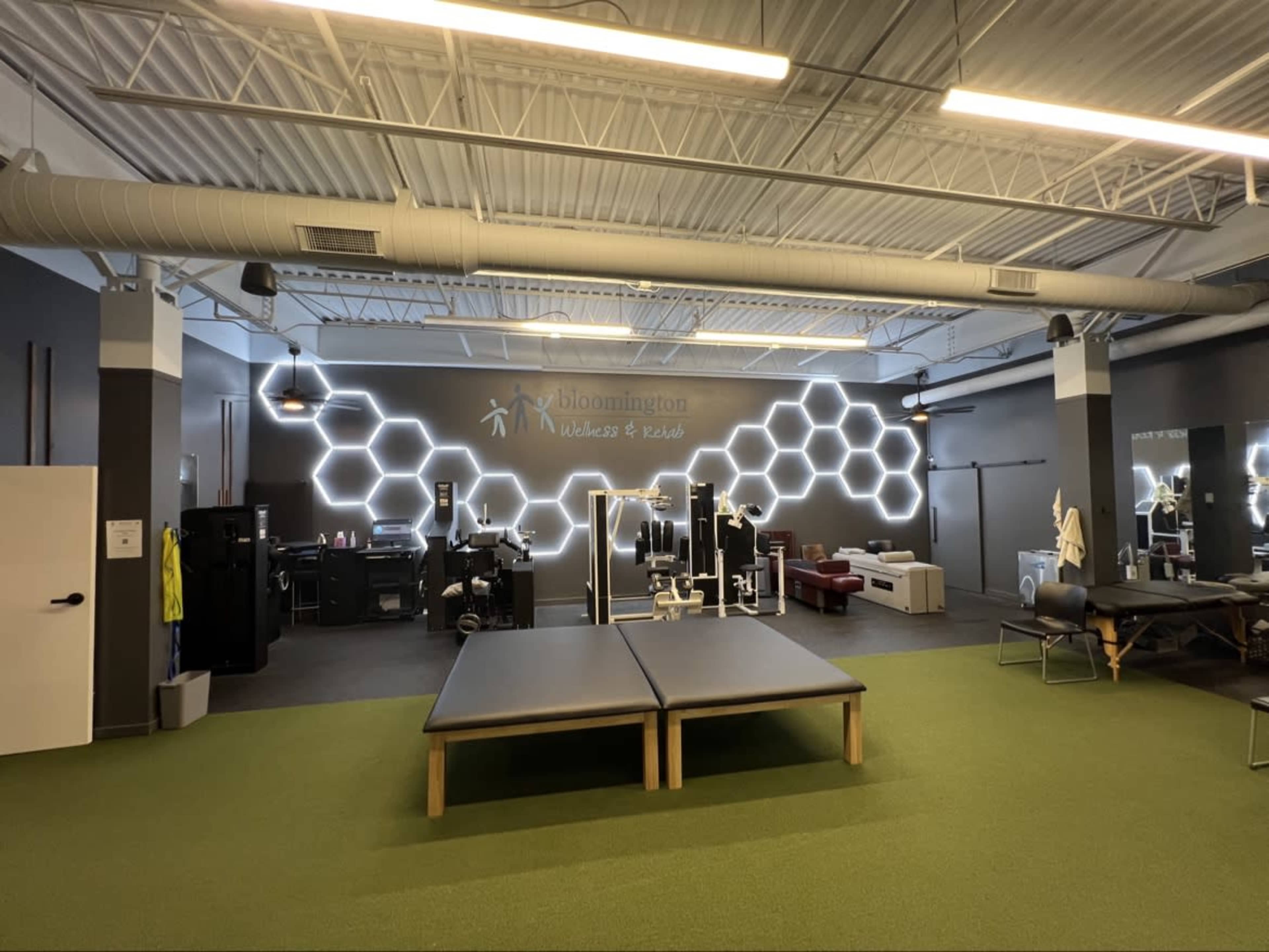 The image shows a fitness and rehabilitation center with exercise equipment and a reception area, featuring a modern design and a hexagonal wall display.