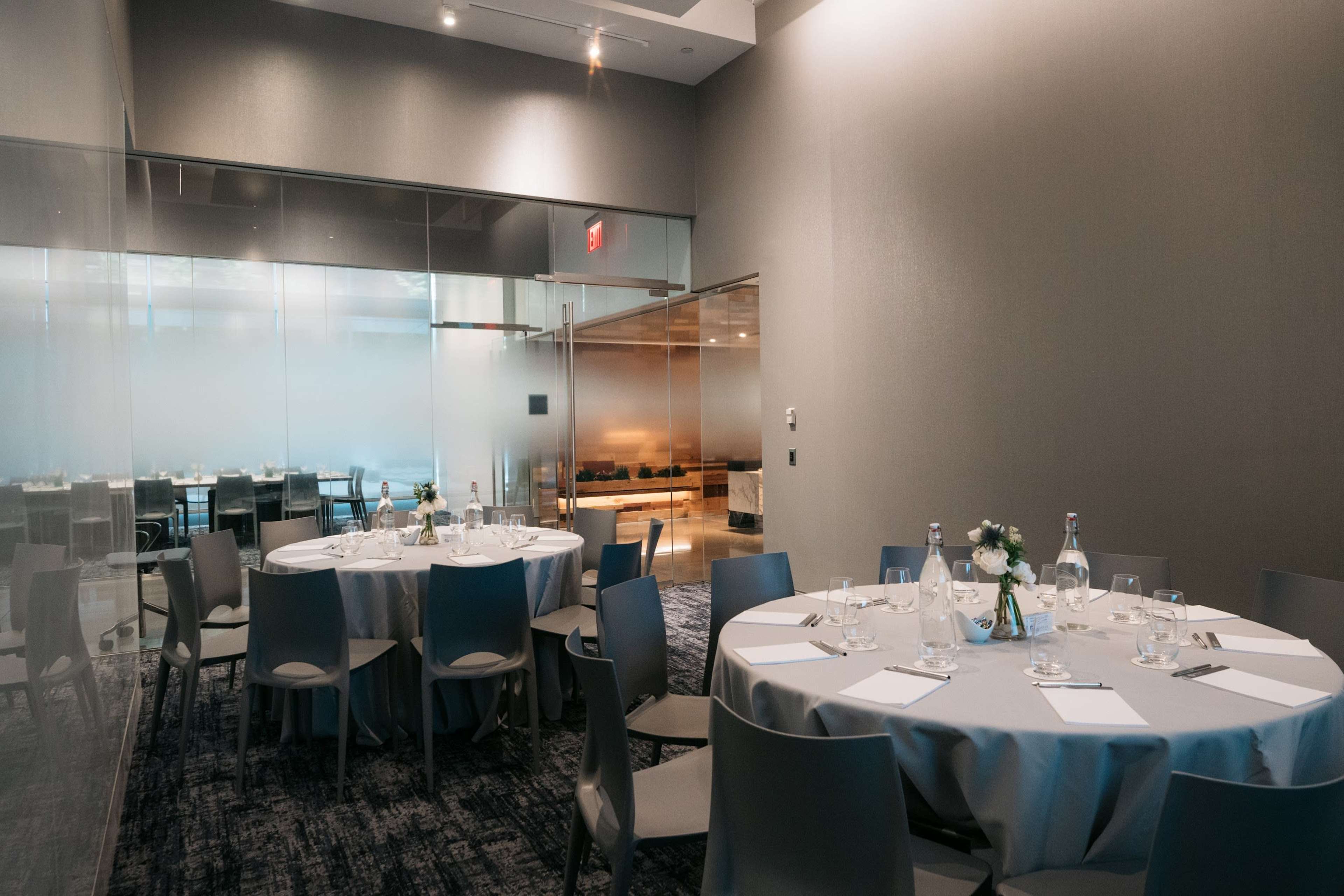The image shows a meeting room with round tables set for an event, featuring gray tablecloths and minimalist decor.