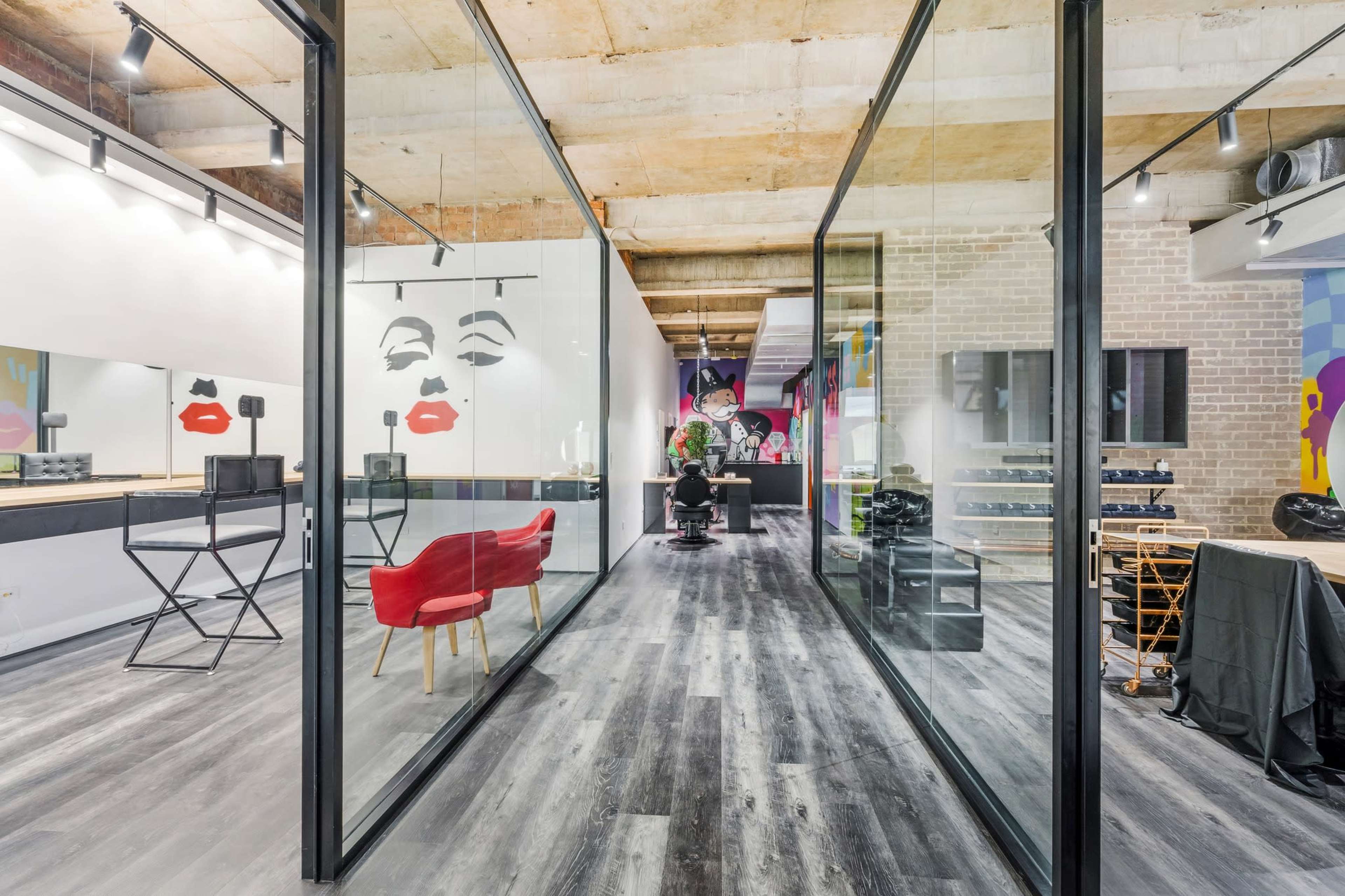 A modern salon interior with glass partitions, featuring colorful wall art and an area with styling stations and furniture.
