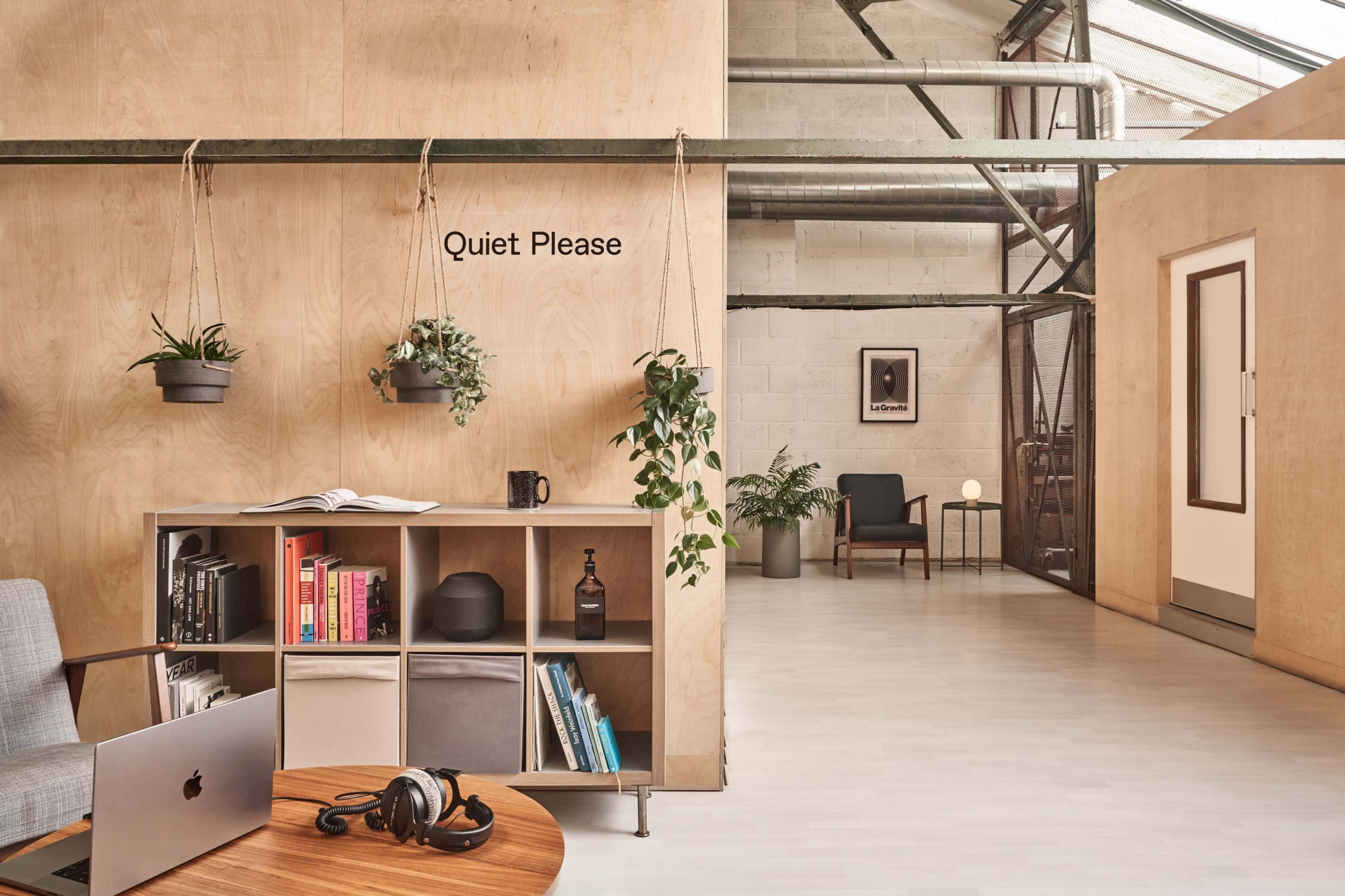 A modern office space with wooden walls, a bookshelf, plants, and a sign reading "Quiet Please."