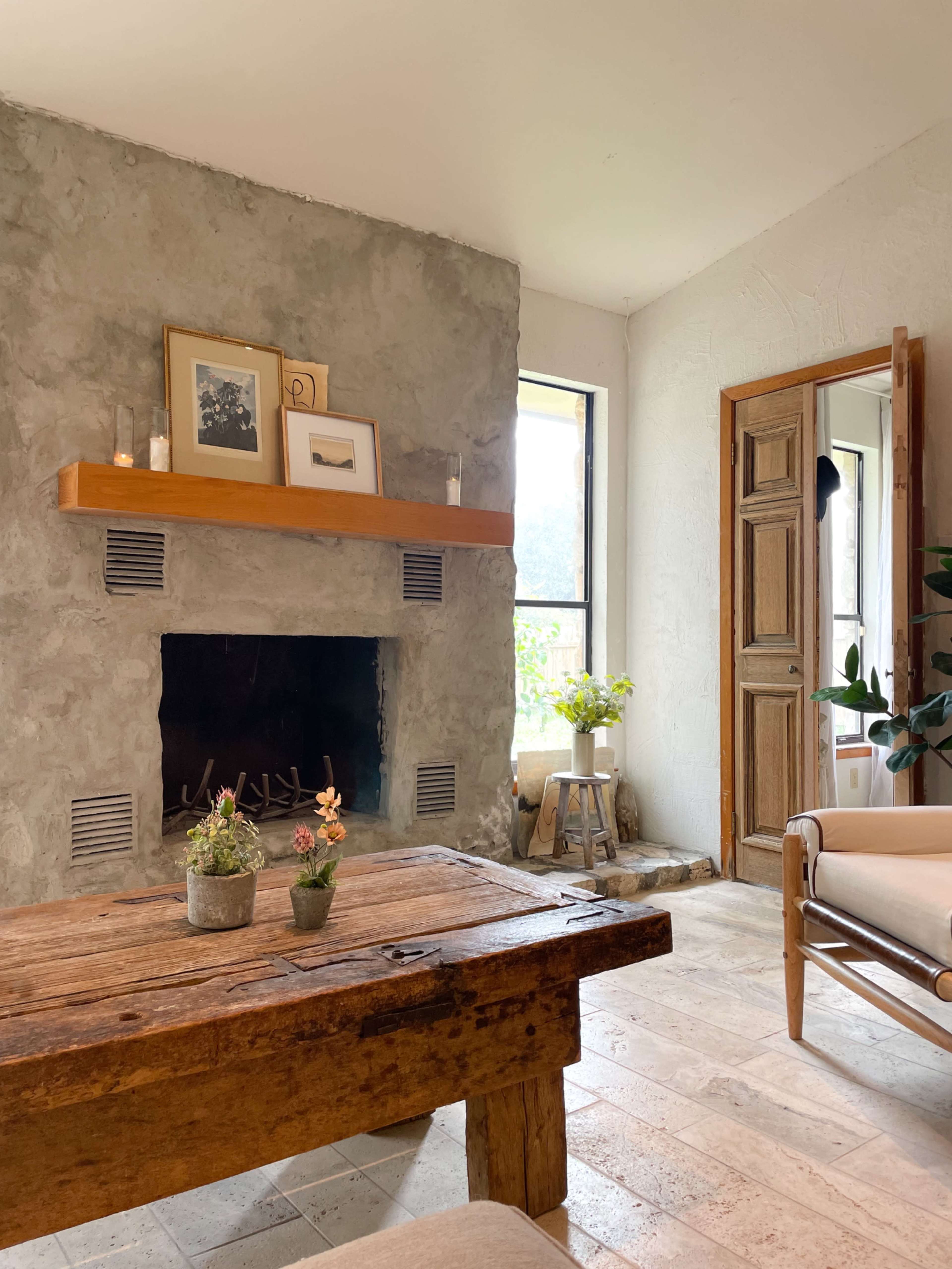 A cozy living room with a stone fireplace, wooden mantel, and a rustic coffee table adorned with small potted plants.