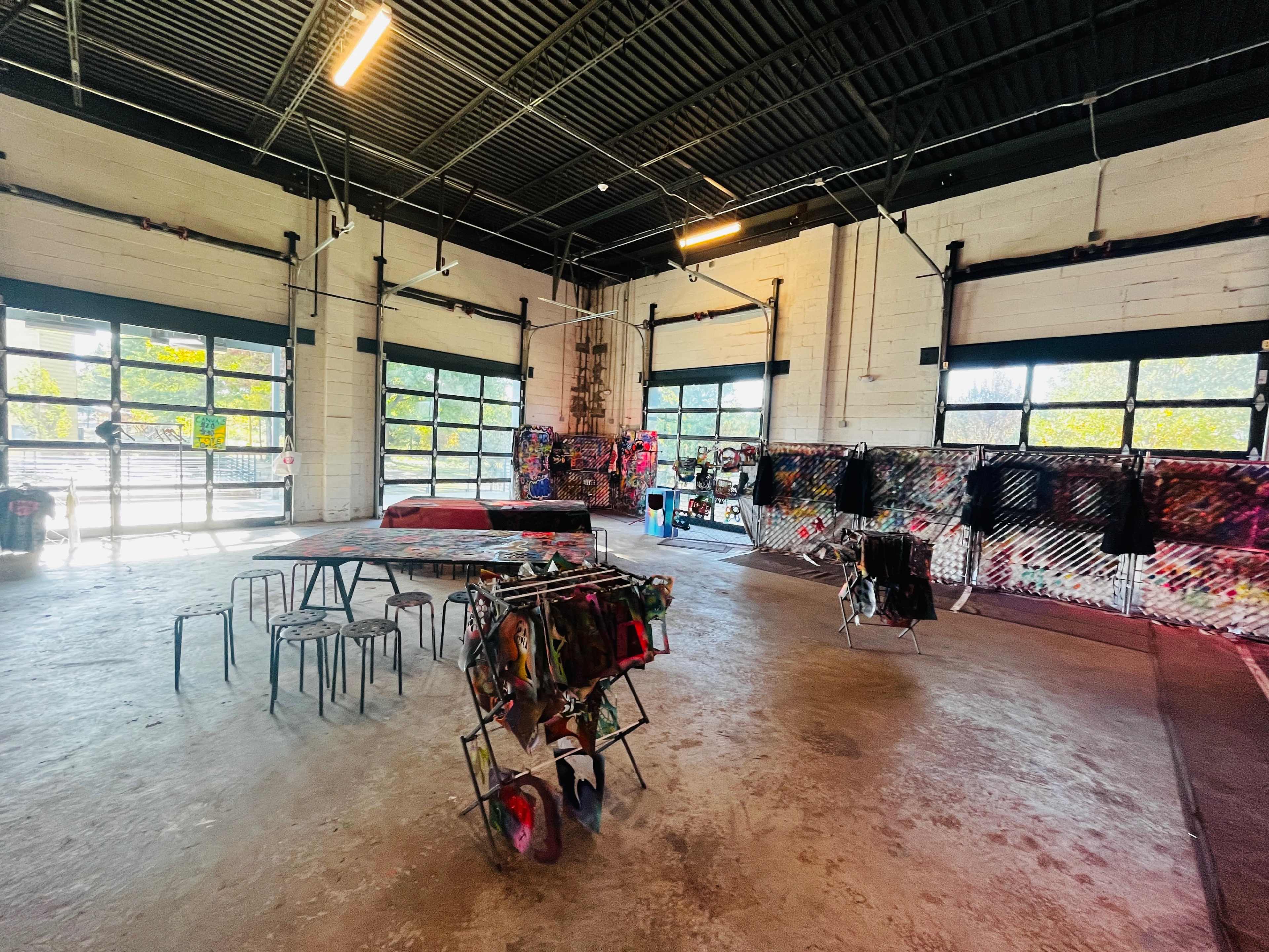 An industrial-style room with concrete flooring, large windows, a few clothing racks, and colorful graffiti on the walls.