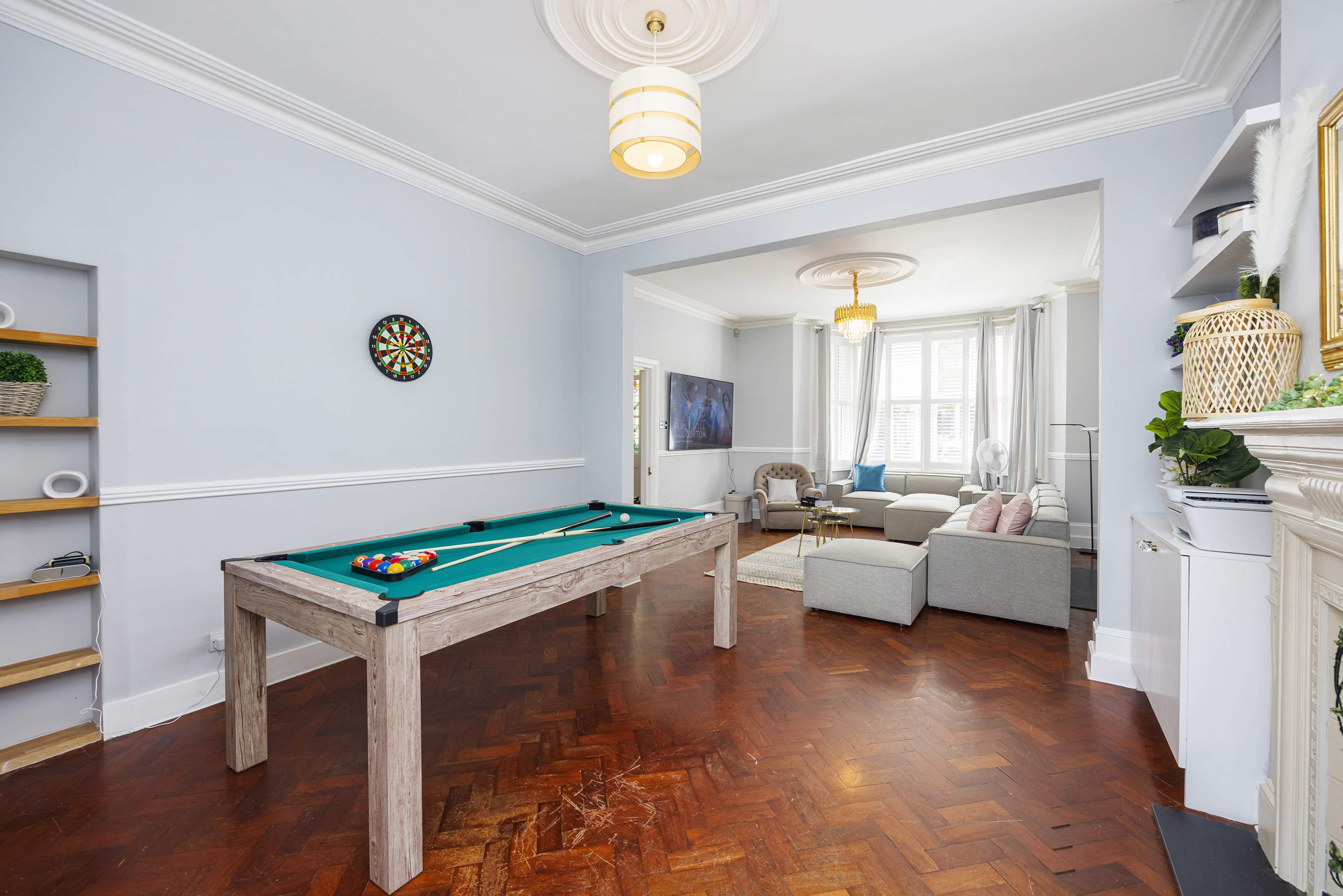A brightly lit living room features a wooden pool table and a cozy seating area with a large window.