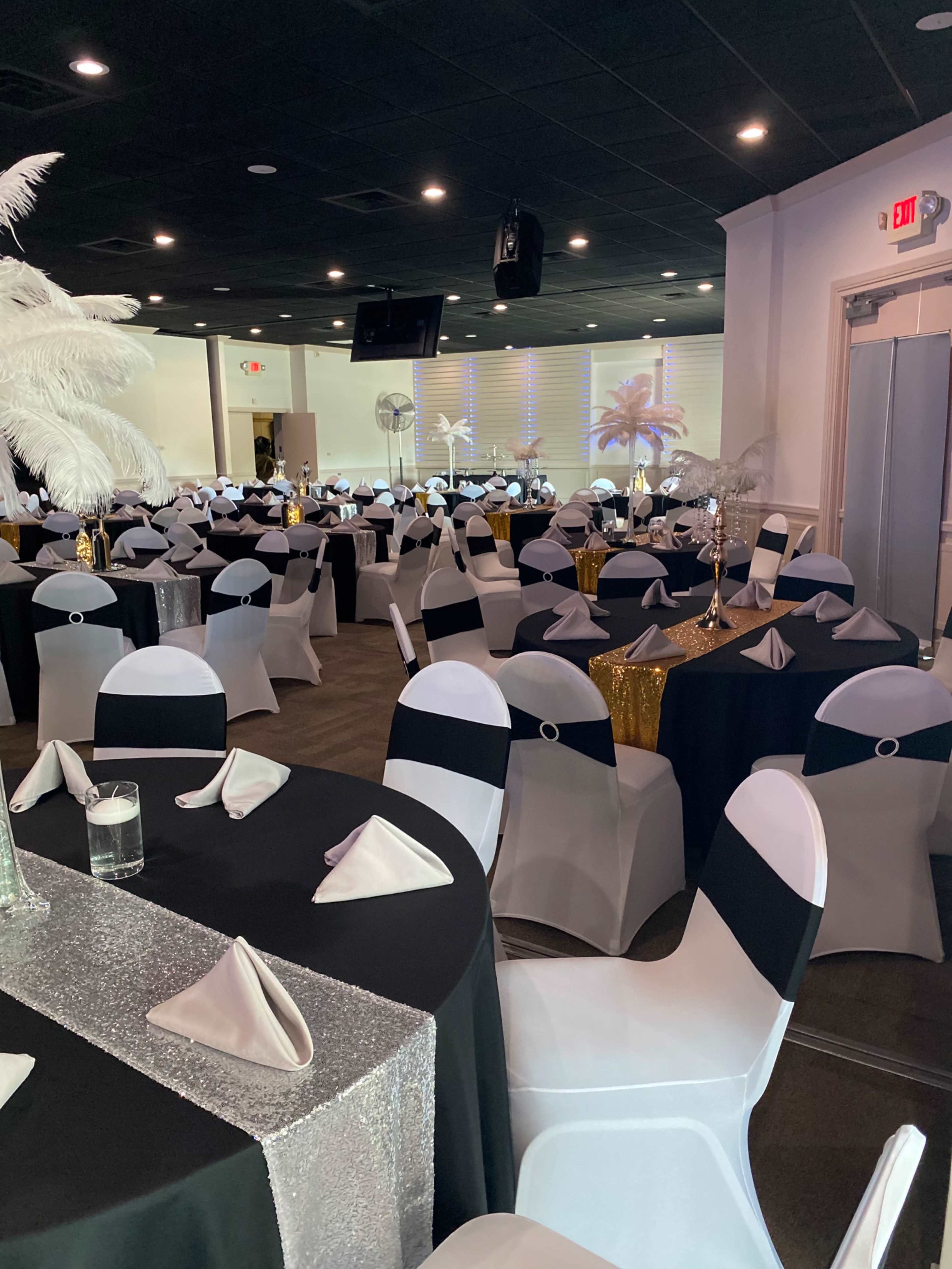 A banquet hall arranged with tables covered in black and white tablecloths and decorated with napkins and centerpieces.