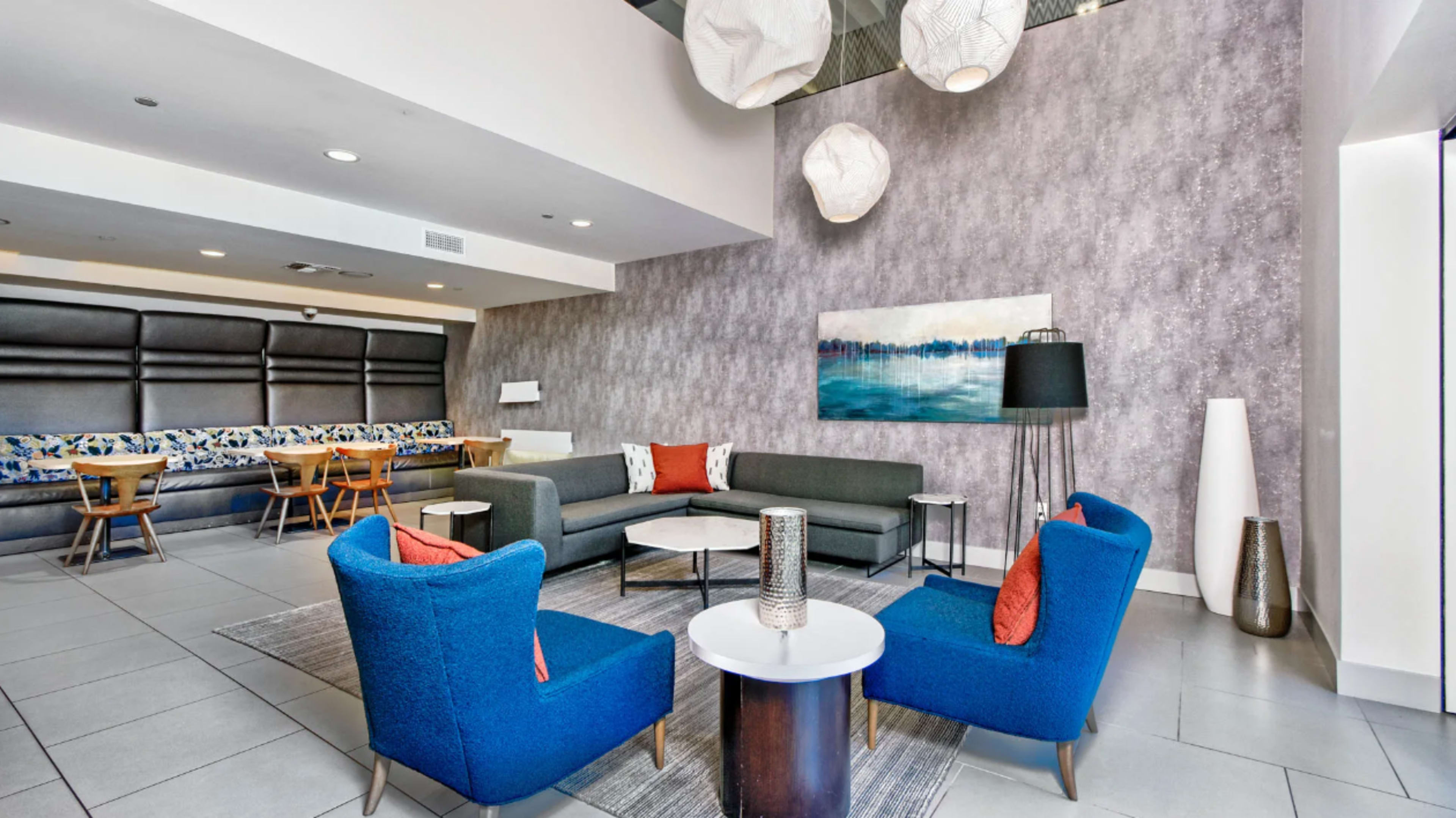 A modern lounge area with a gray wall, blue chairs, a sofa, a coffee table, and decorative light fixtures.