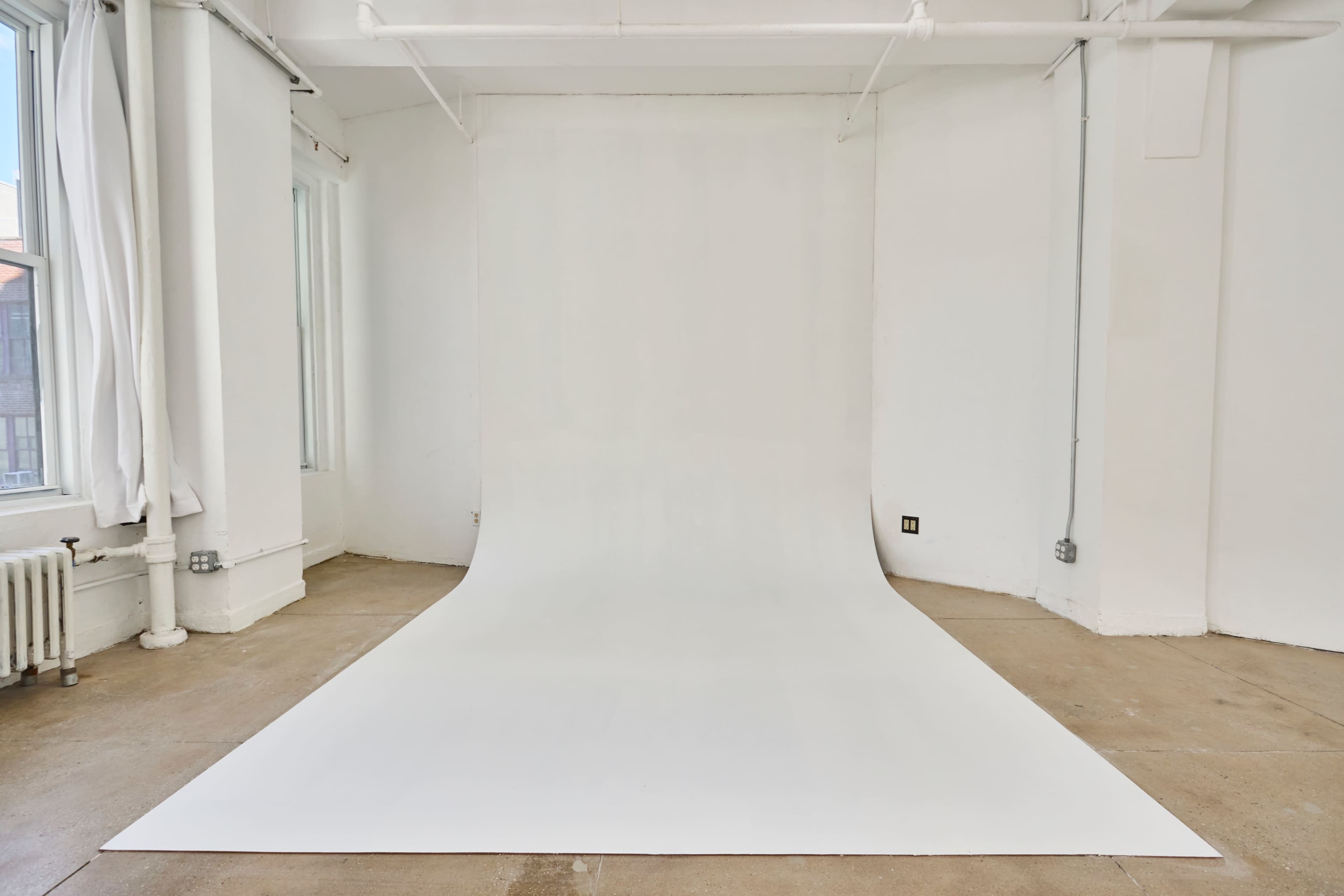 The image shows a spacious, empty room with white walls and a seamless white backdrop extending to the floor.
