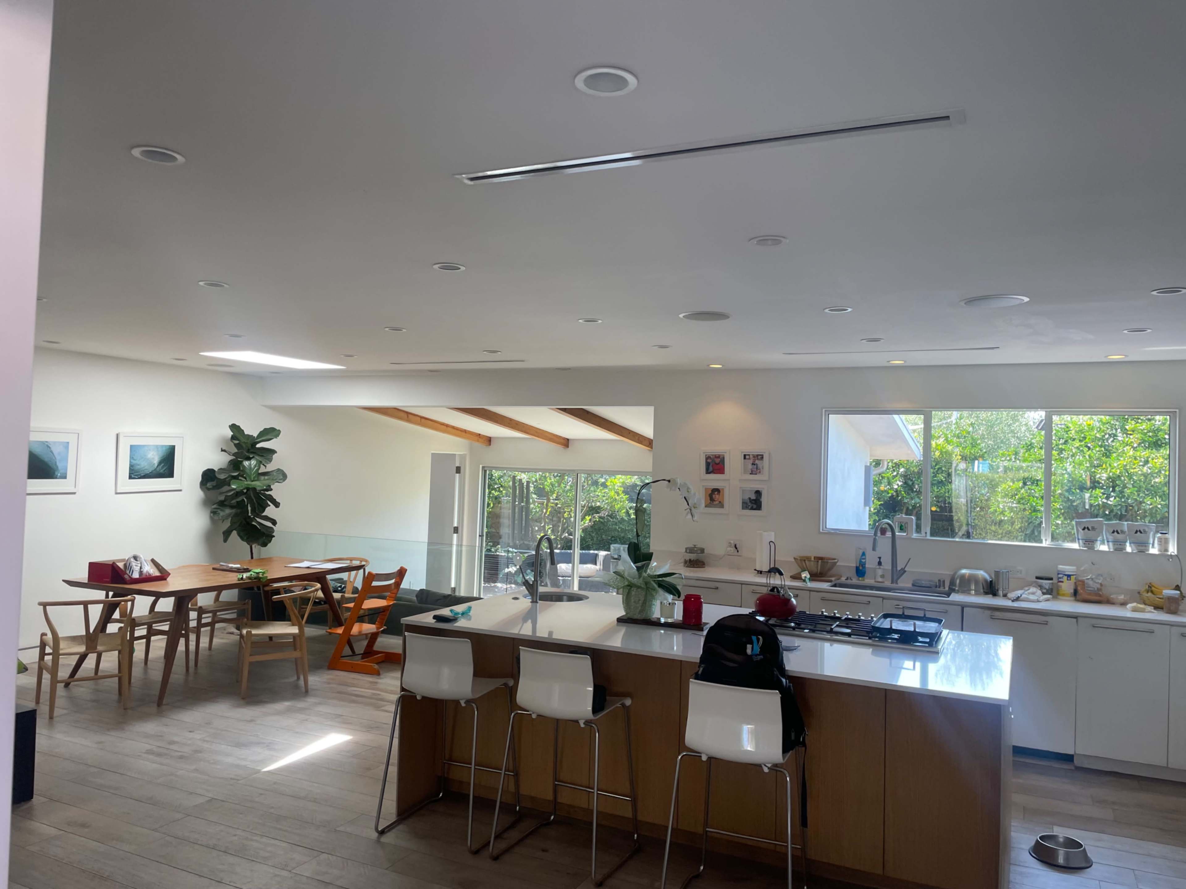 A modern kitchen and dining area featuring a large island, wooden dining table, and large windows with greenery visible outside.